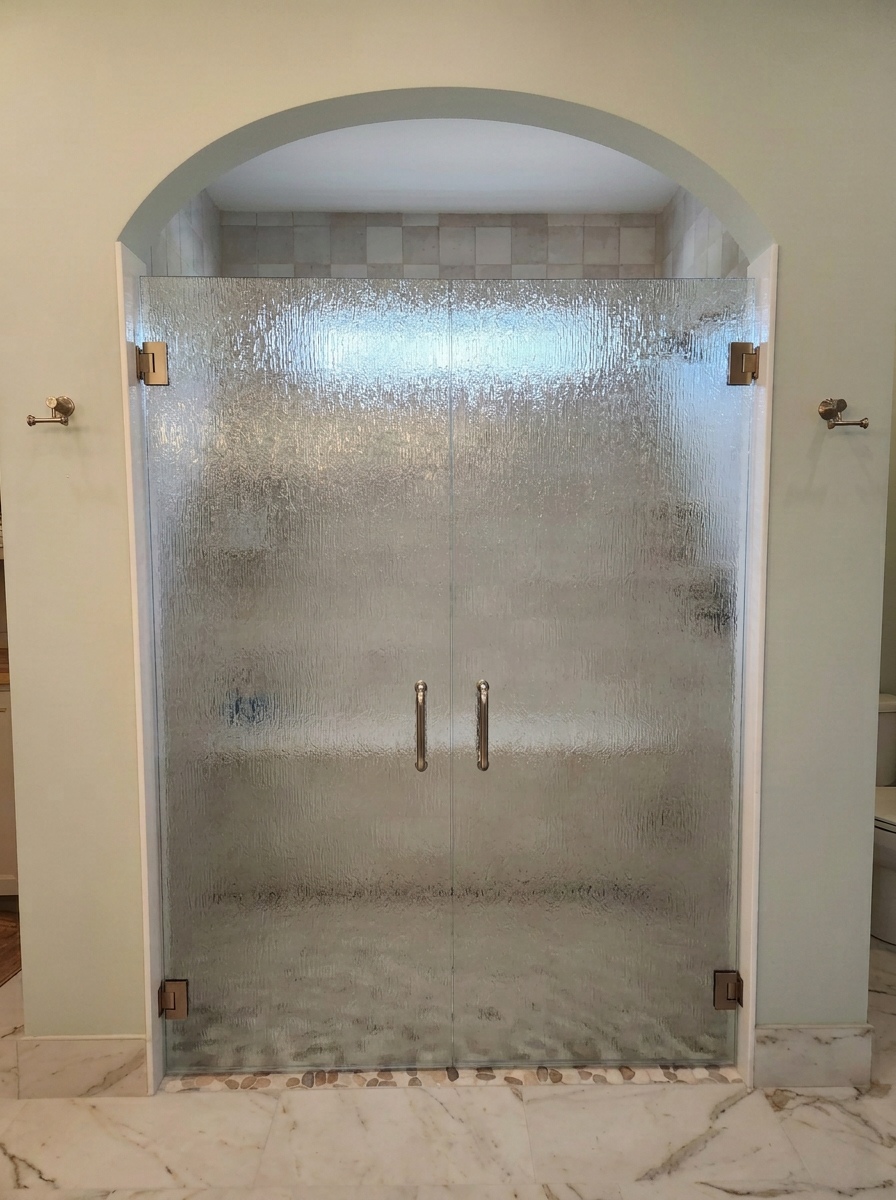 Glass shower door with metal handles in a bathroom with marble floor and tiled wall.