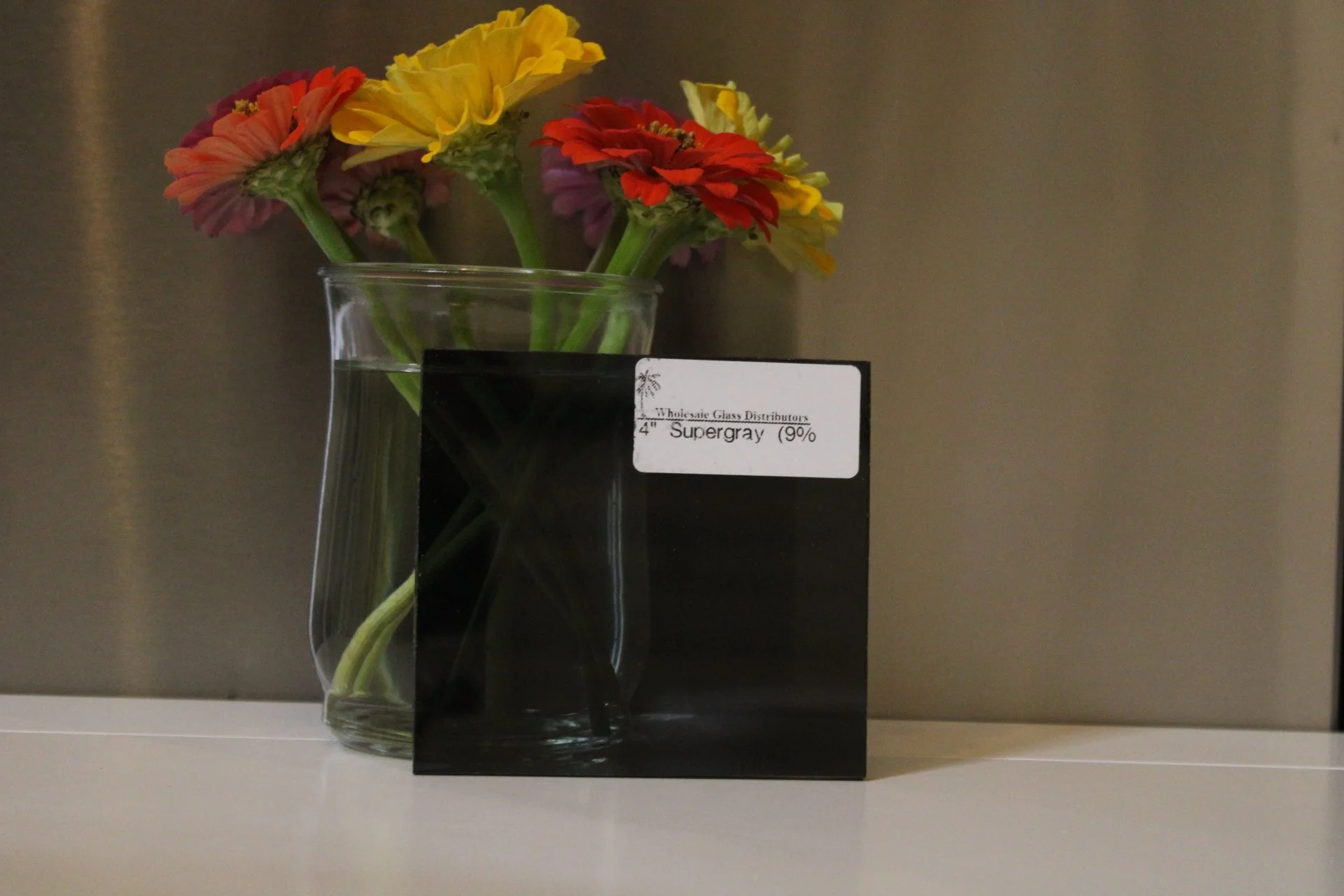 Colorful flowers in a glass vase placed on a black box, with a label indicating they are Supergray flowers.