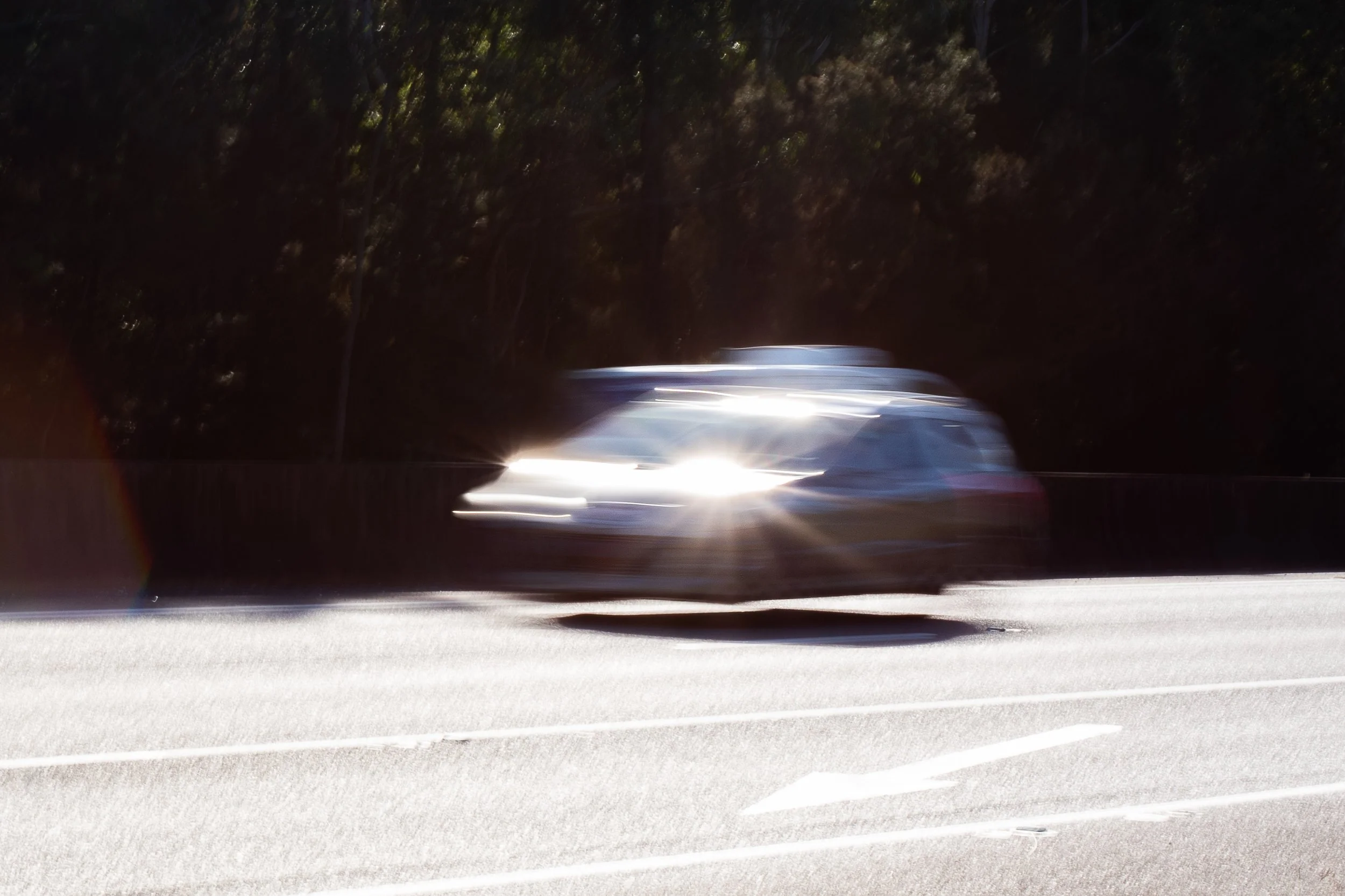 A white car driving at night on a road with trees in the background, with motion blur and bright headlights.