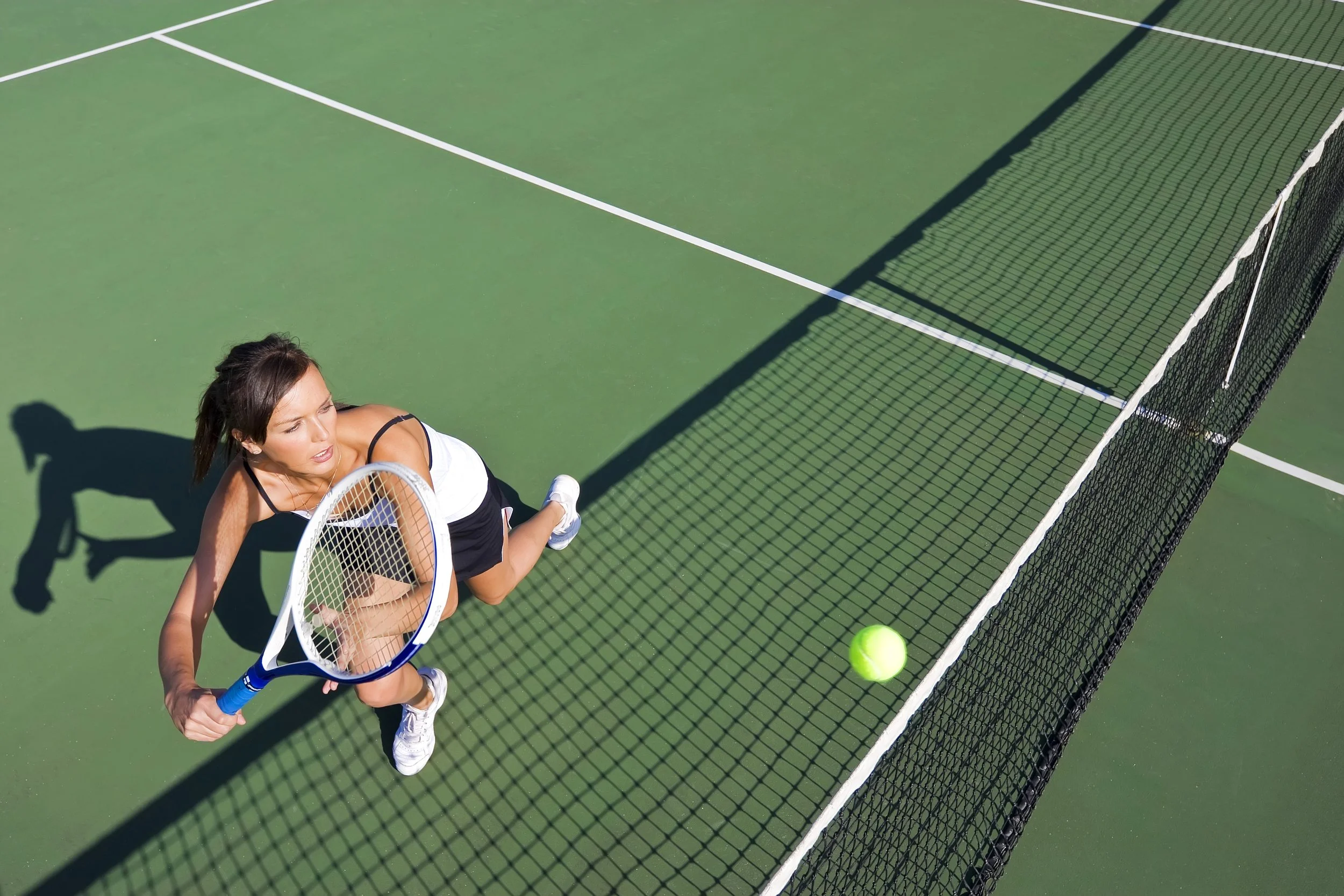 A female tennis player in a black and white outfit preparing to hit a tennis ball on a green court with a net.