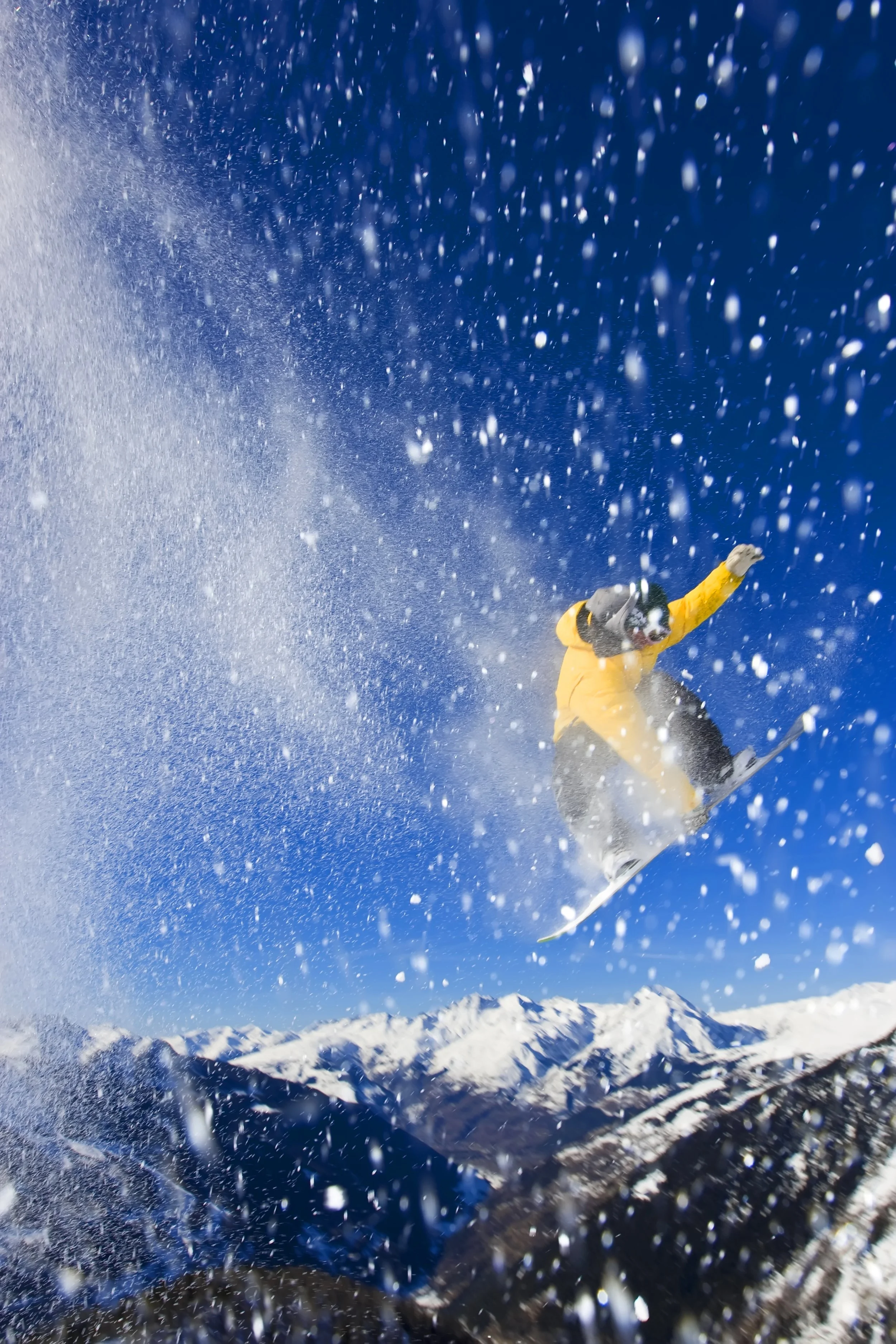 A person in yellow and black winter gear skiing downhill on a snowy mountain with a blue sky and distant mountain peaks in the background.