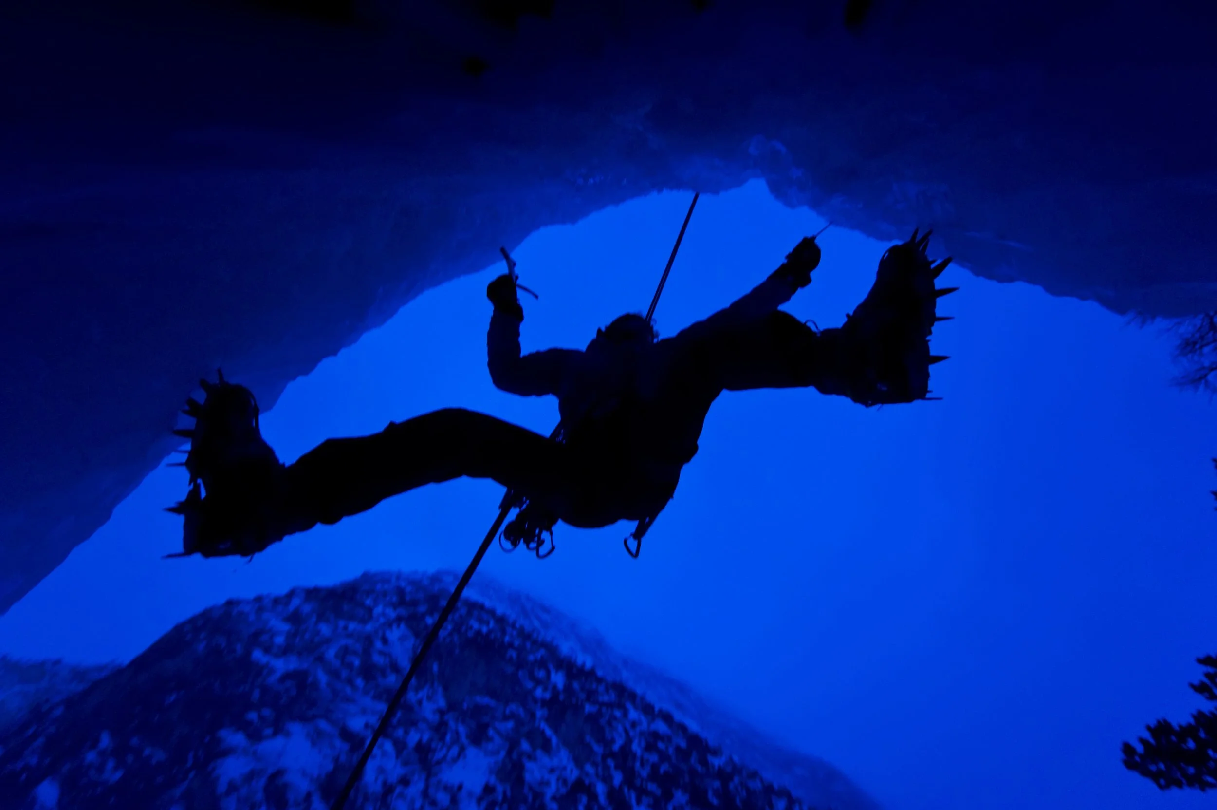 Silhouette of a person climbing or rappelling on a cliff or mountain at night with a blue sky background.