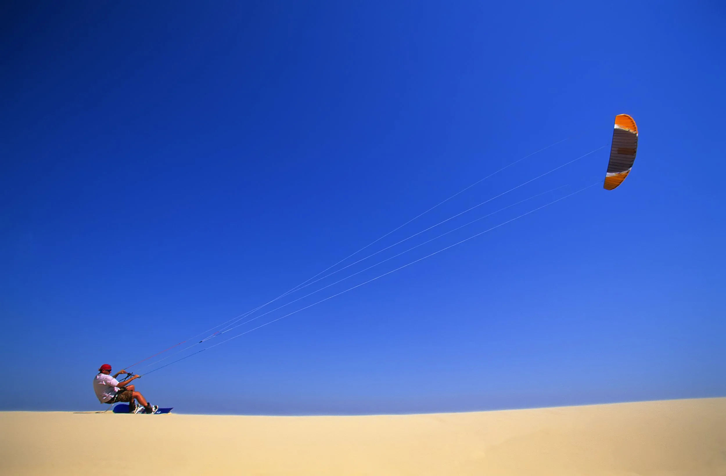 Person flying a kite on a sandy beach with a clear blue sky.
