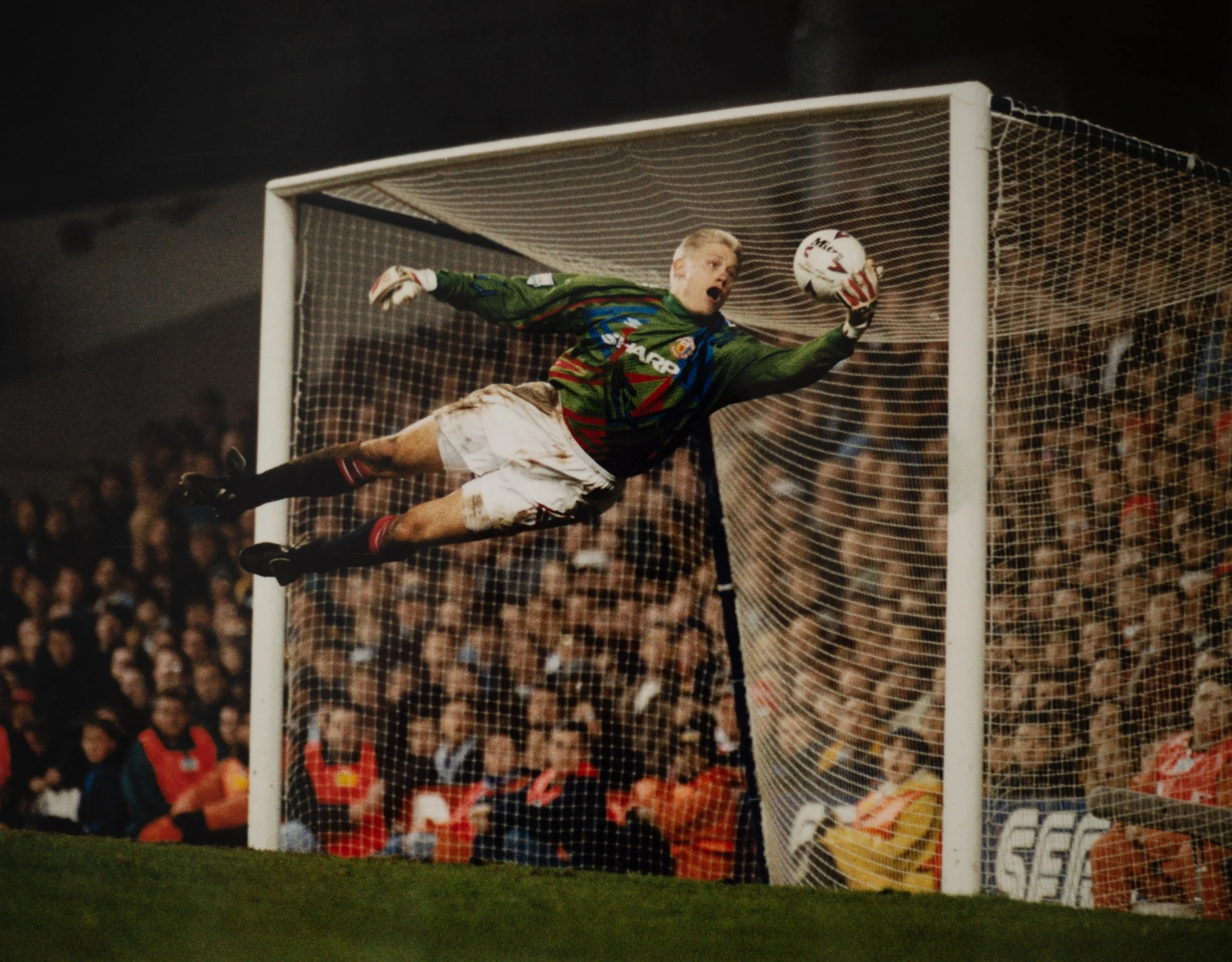 Soccer goalkeeper in green uniform making a save during a match in a stadium full of spectators.
