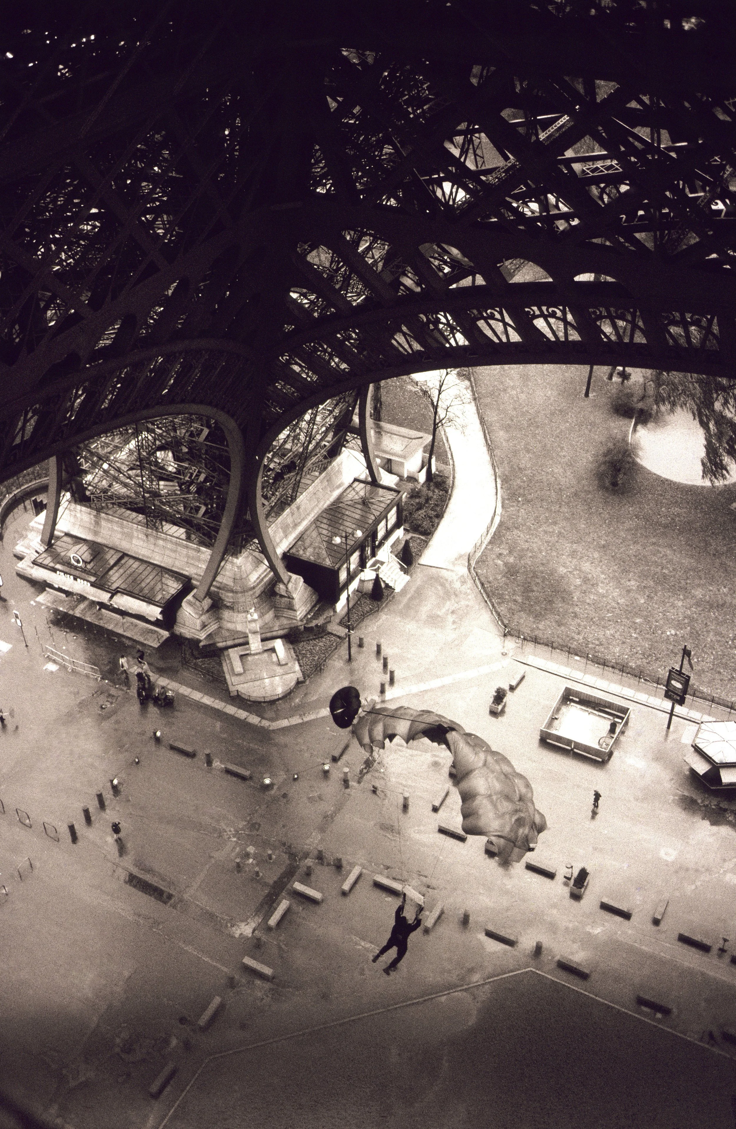 Nighttime view of the Eiffel Tower showing its intricate iron lattice structure from below, with a nearby park and few people walking.