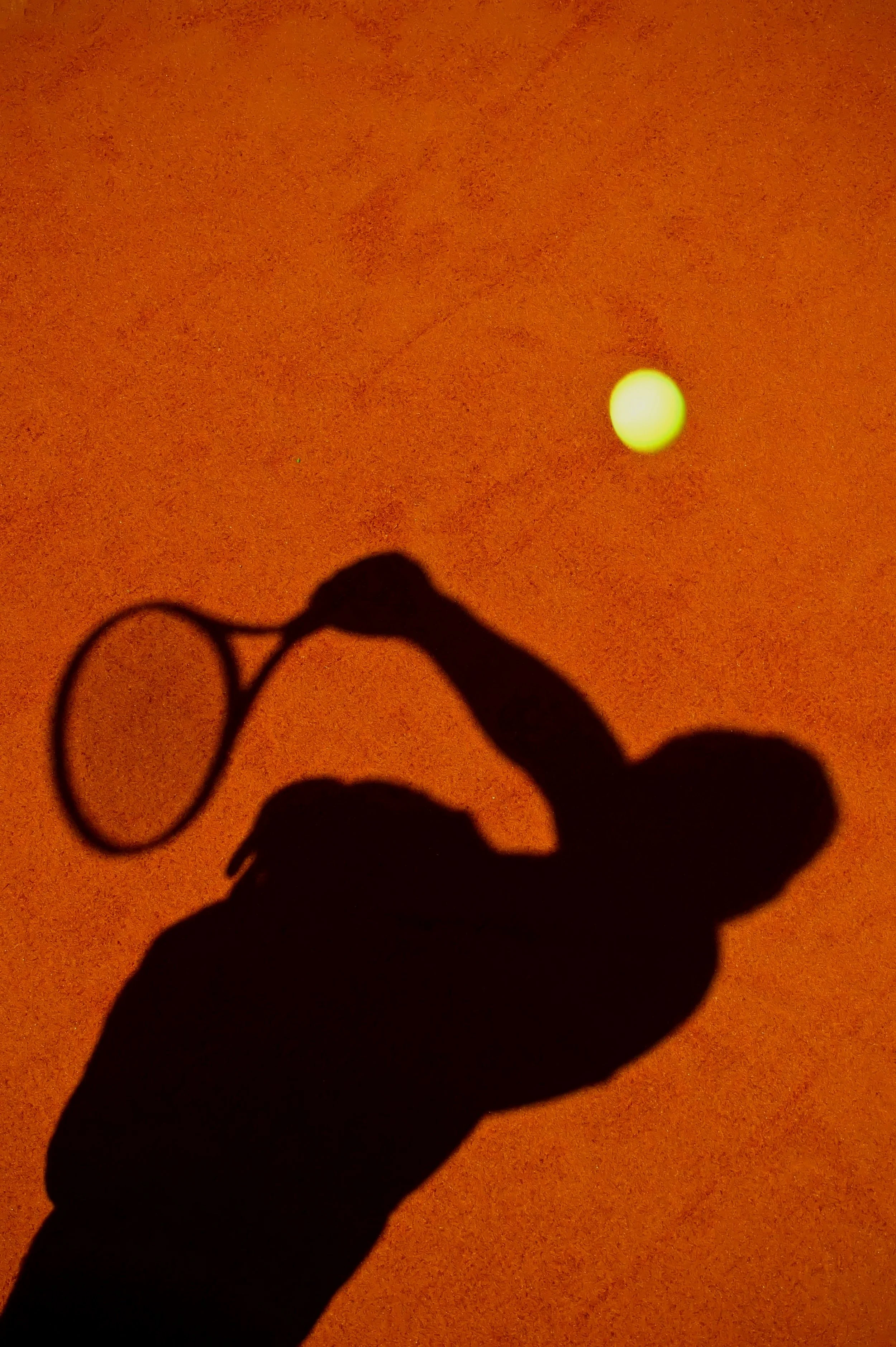 Silhouette of a hand holding an object against an orange background with a bright circular light.