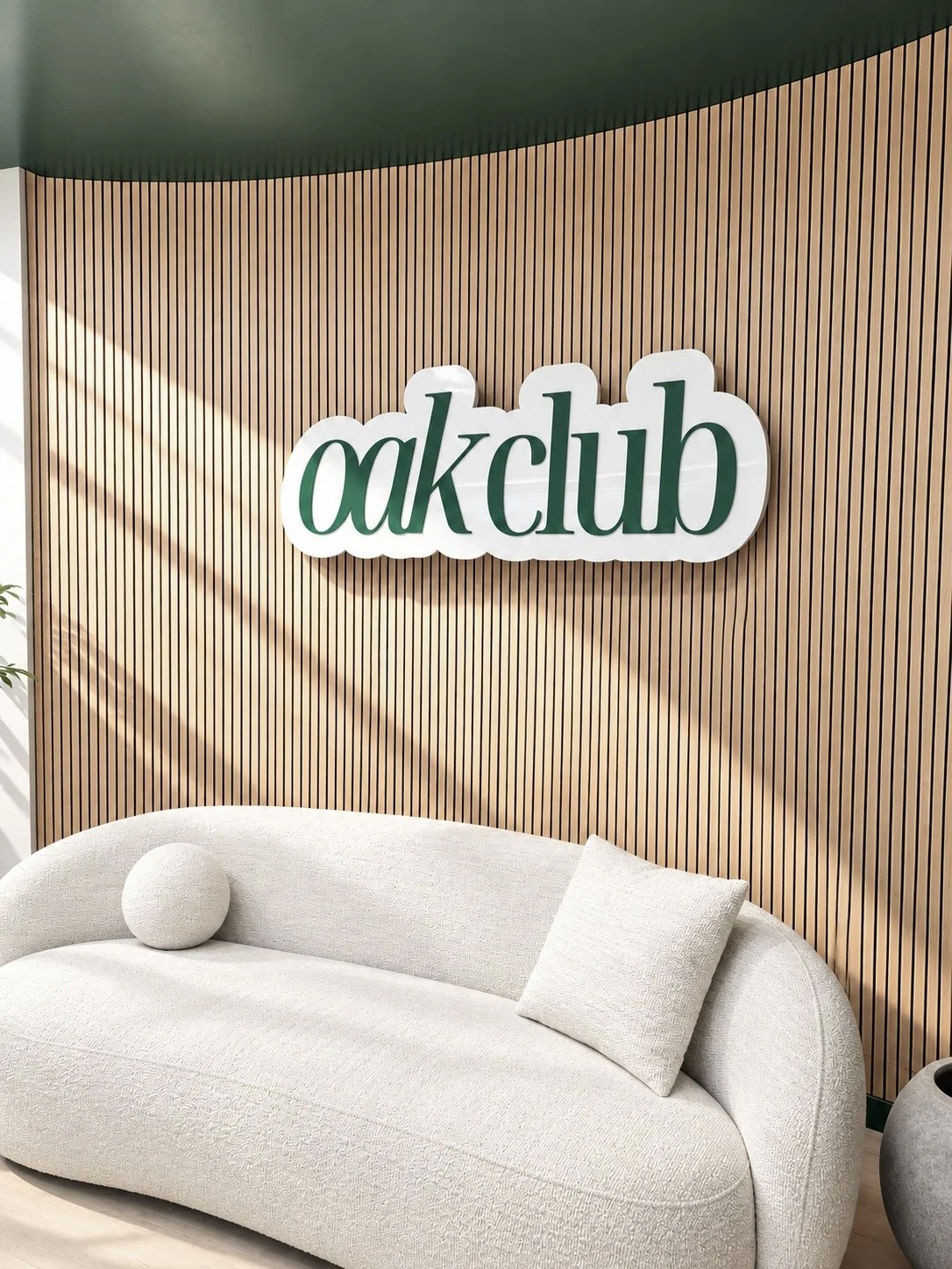 Interior of a modern lounge with a white curved sofa, decorative pillows, and a wooden slat wall featuring a sign that says 'oakclub' in green letters.