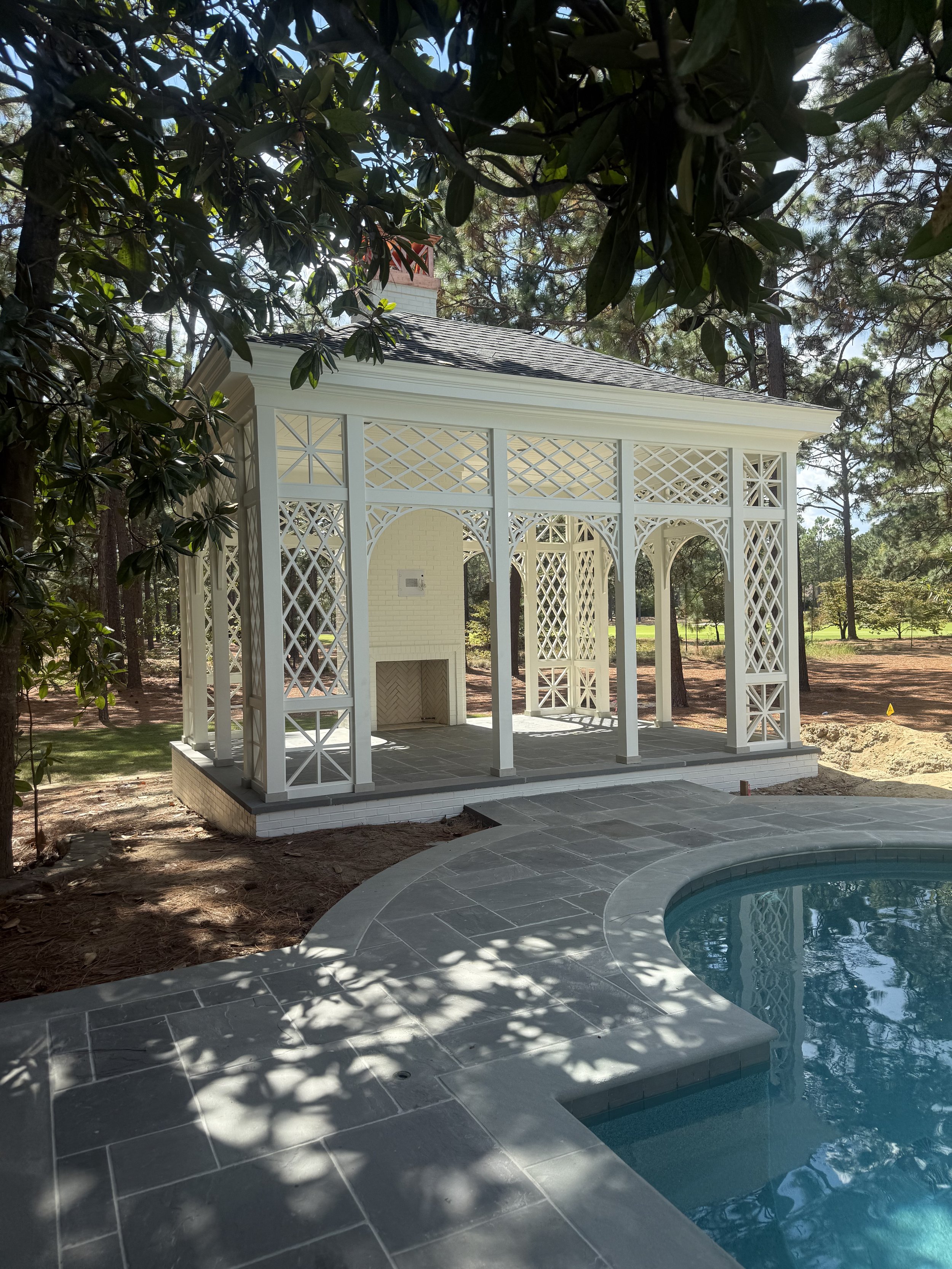 A backyard with a white gazebo near a swimming pool surrounded by trees and greenery.