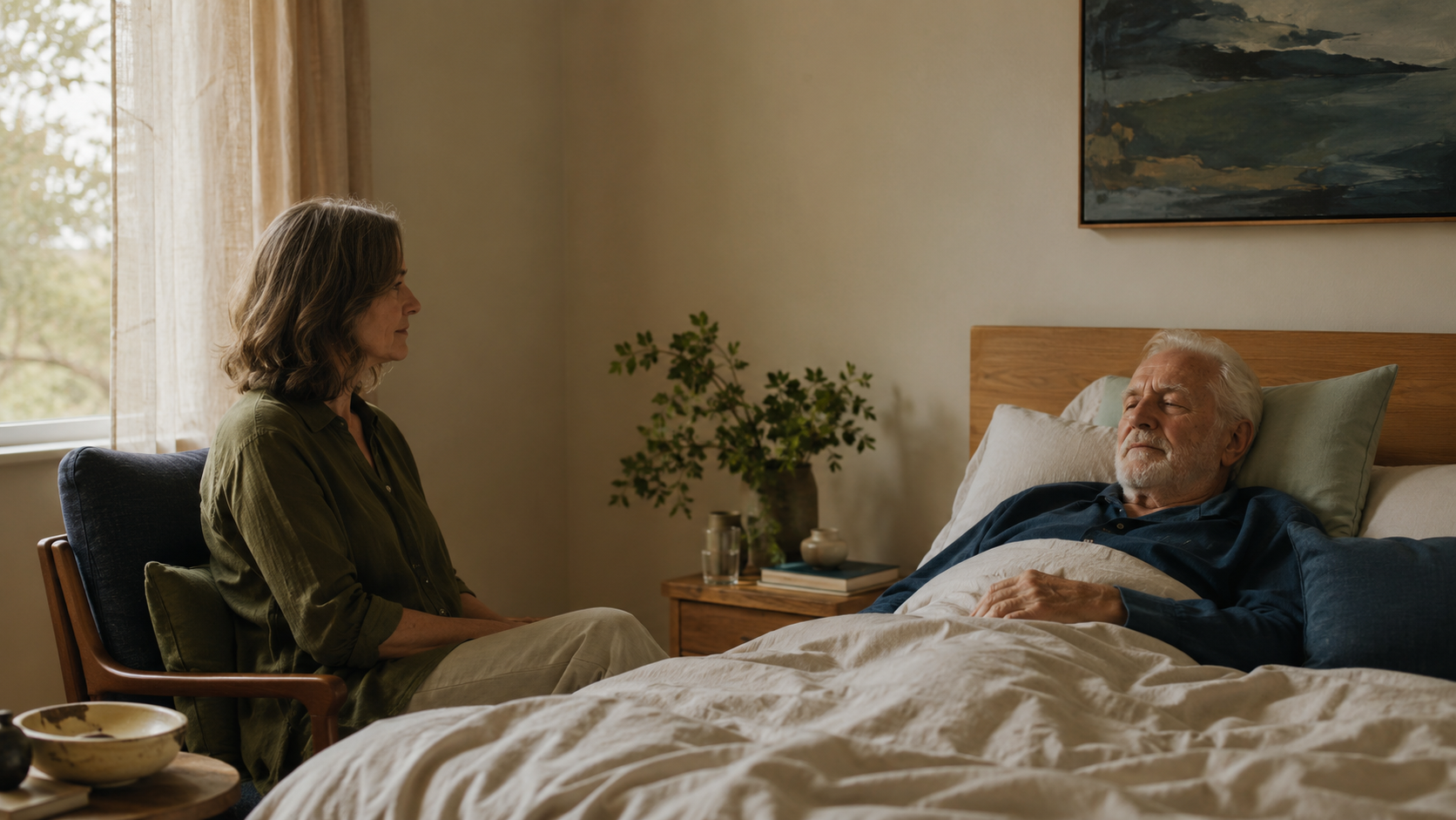 A volunteer sitting quietly beside an older man resting at home.