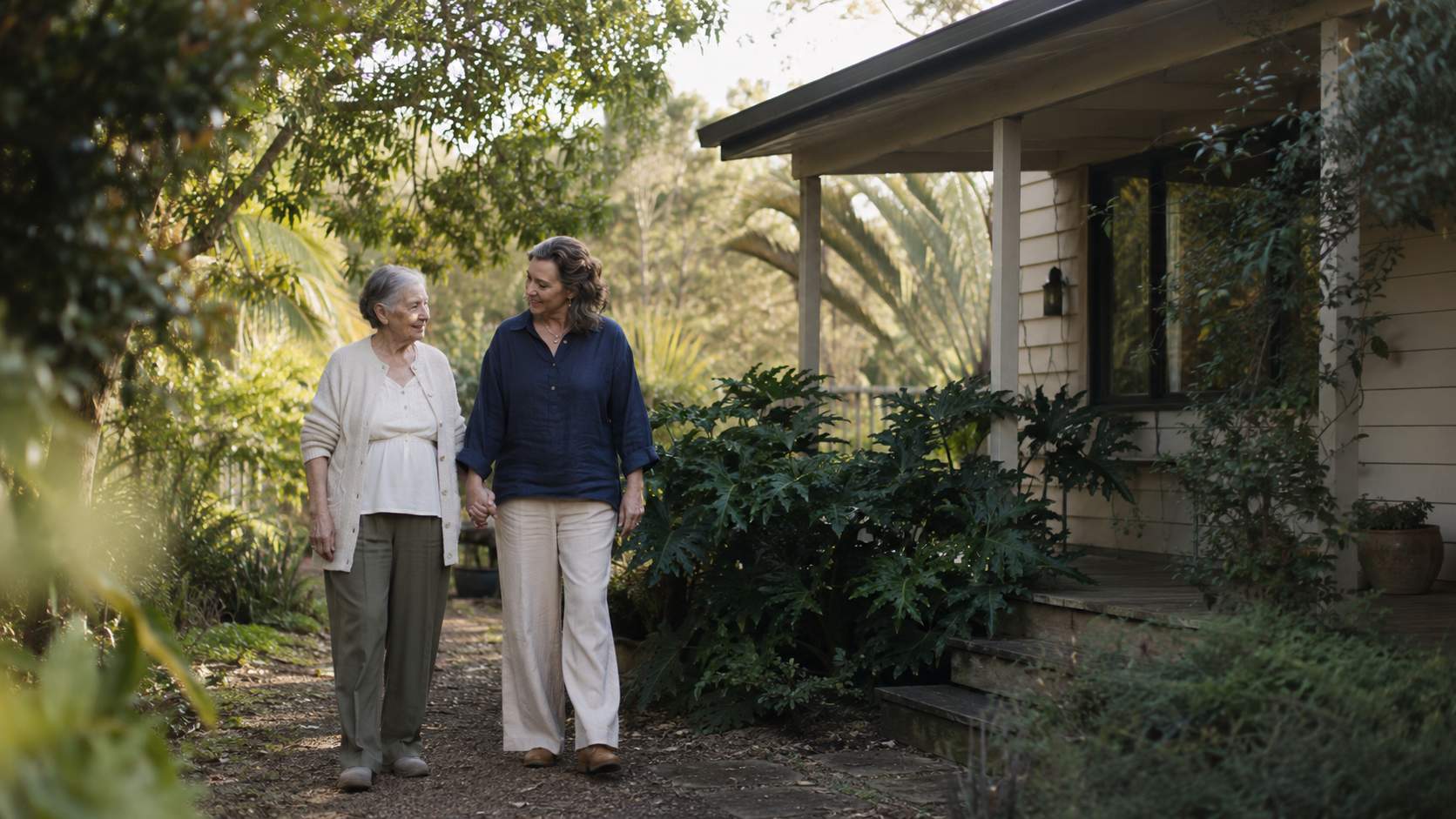 A volunteer walking beside an older woman along a garden path at home.