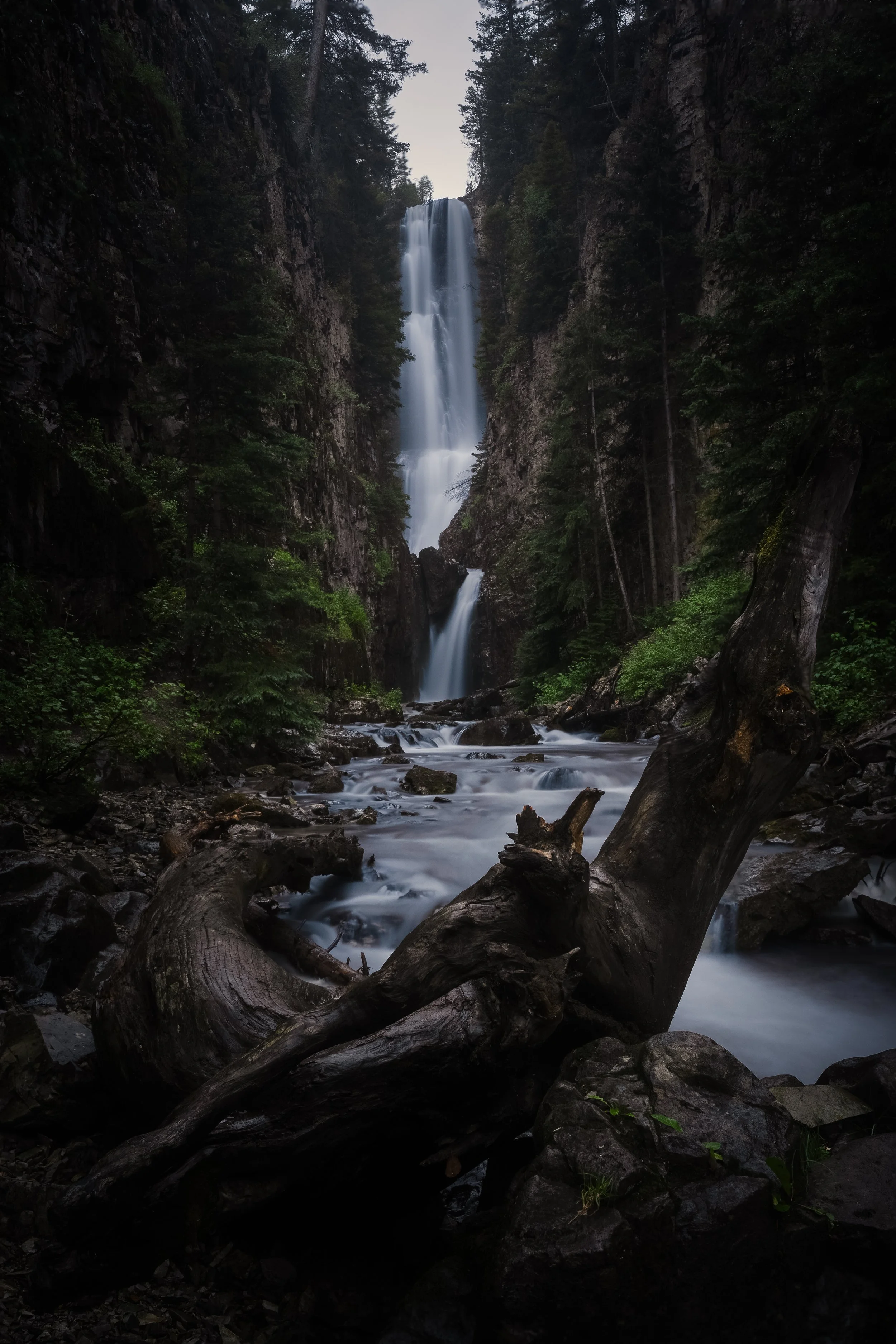 Tall waterfall flowing between large rocks and tall trees in a forest.
