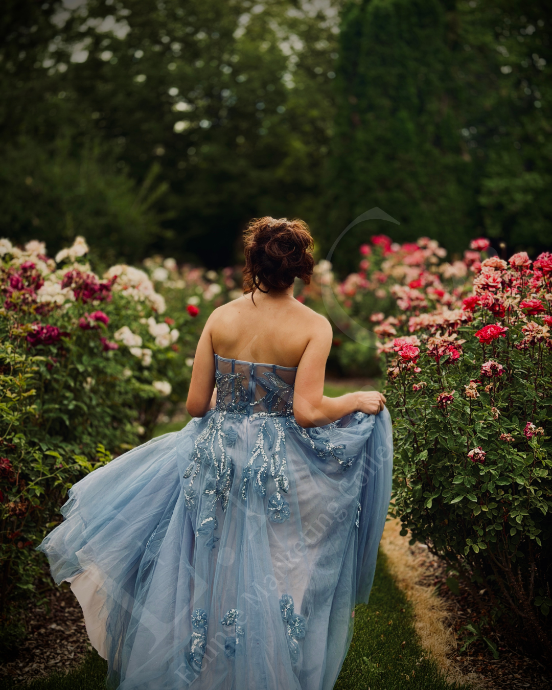 Woman in a light blue, strapless, embroidered gown walking through a garden with pink and white roses.