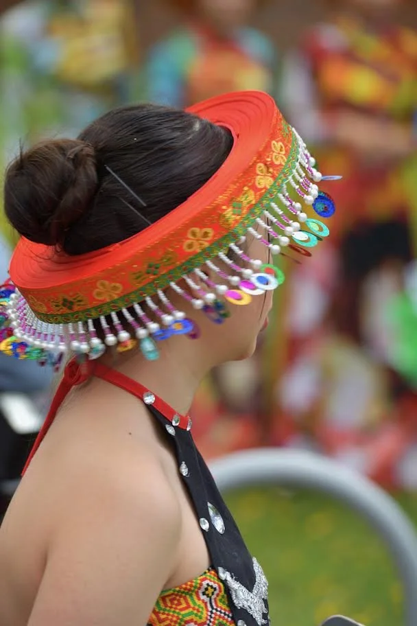 Woman in traditional colorful embroidered headwear with dangling bead ornaments and a black embroidered garment