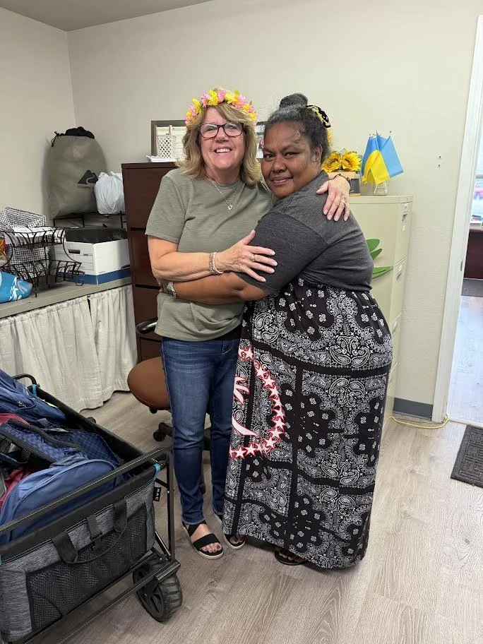 Two women smiling and embracing in an office, with Ukrainian flags and storage equipment in the background.