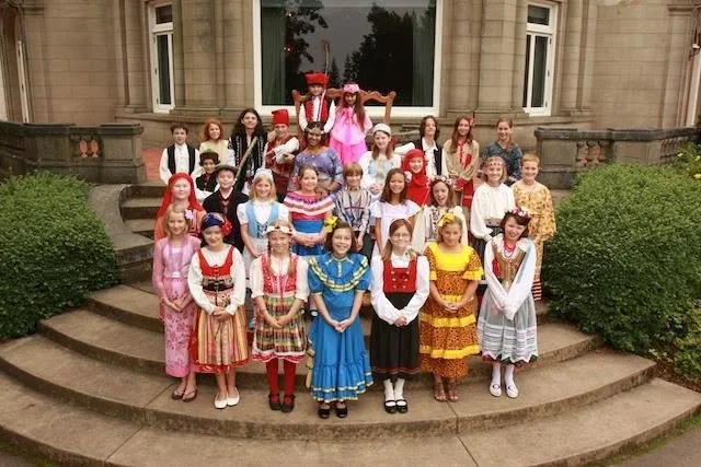 Group of children in colorful traditional costumes posing on the steps of a building.