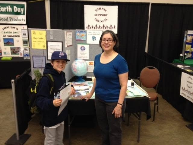 Woman and young boy at an Earth Day environmental education booth with posters, brochures, and a globe