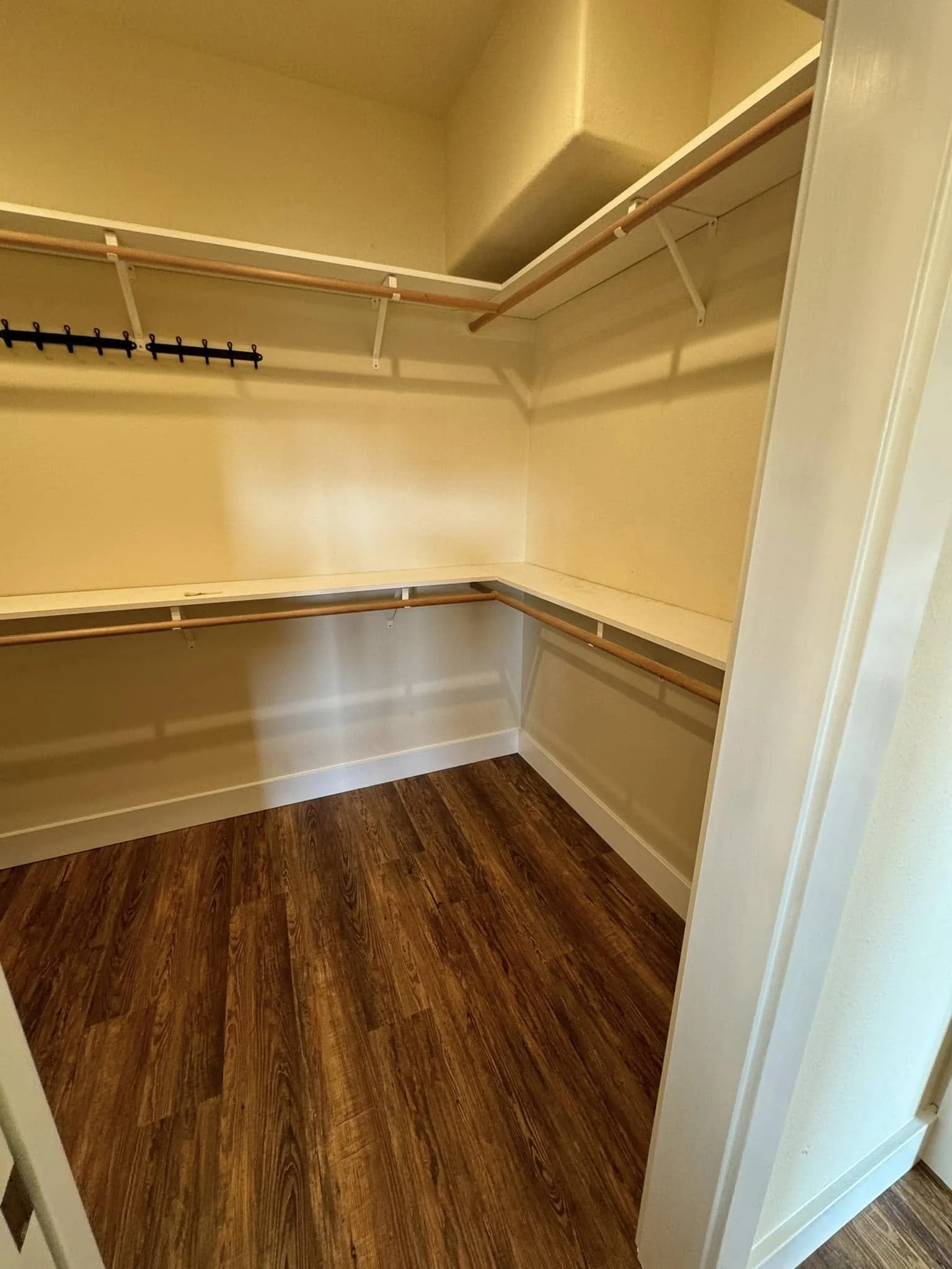 Empty walk-in closet with wooden flooring, beige walls, and multiple shelves and clothing rods.