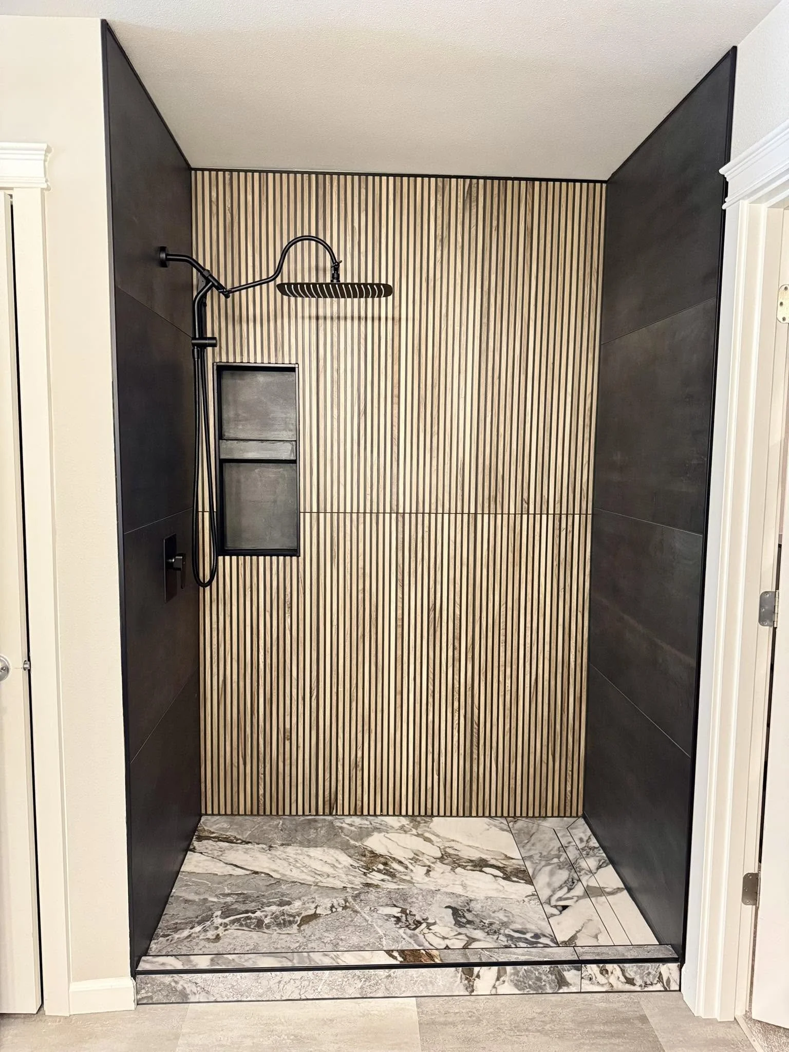 Modern walk-in shower with black fixtures, vertical wooden slat wall, and marble floor tiles.