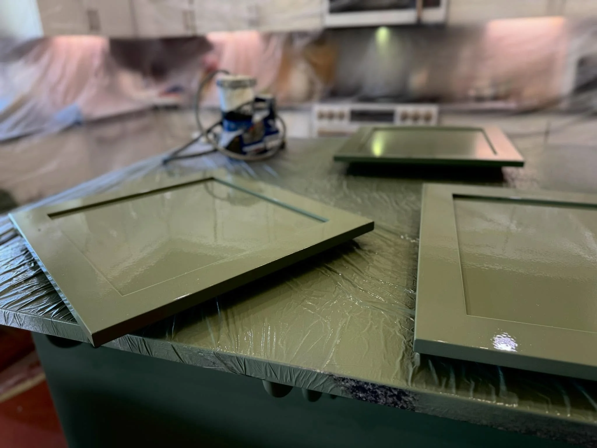 Green metallic sheet with cutout sections, placed on a table covered with protective foil, kitchen setting in the background.