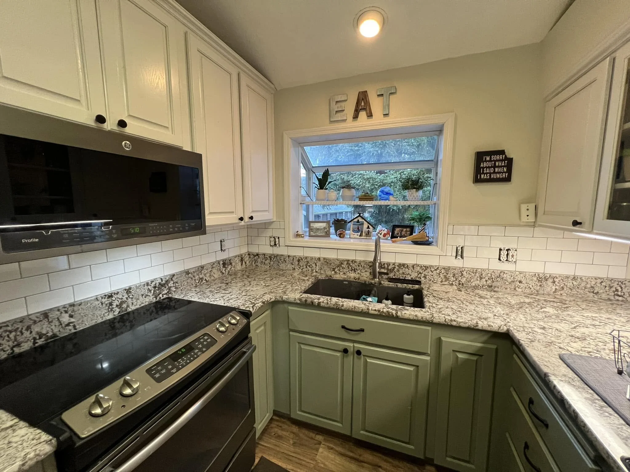 Kitchen with green cabinets, a granite countertop, window with decorative items, and a stainless steel stove.