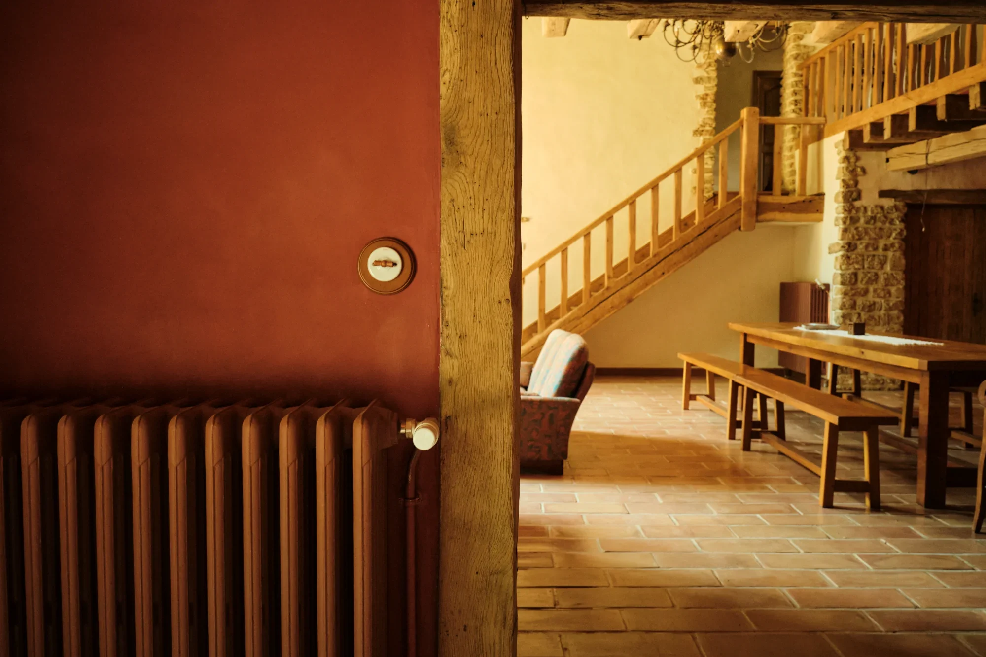 Intérieur d'une maison rustique avec murs en pierre, escalier en bois, mobilier en bois et sol en briques, vue depuis l'entrée.