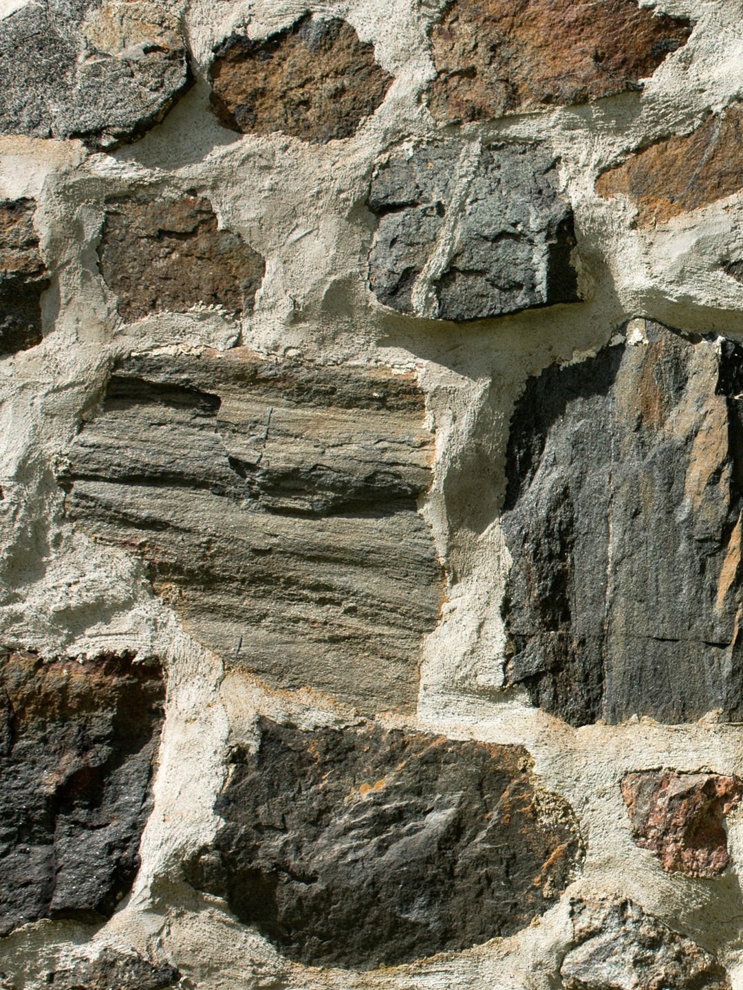 Close-up view of a schist wall with variously sized and textured stone, bagged mortar finish.