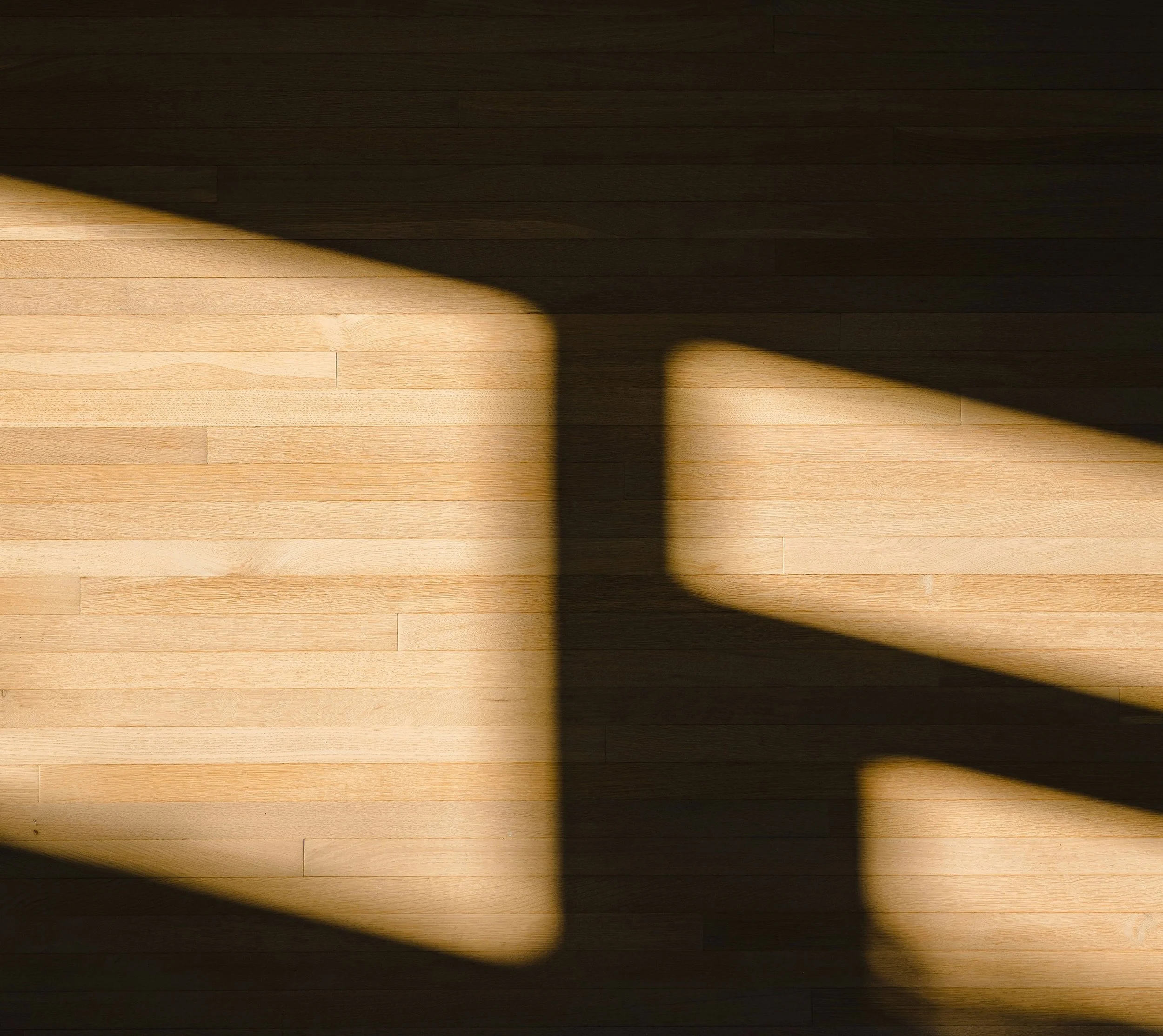 Sunlight casting shadow on light-colored wooden floorboards with visible grain and texture.