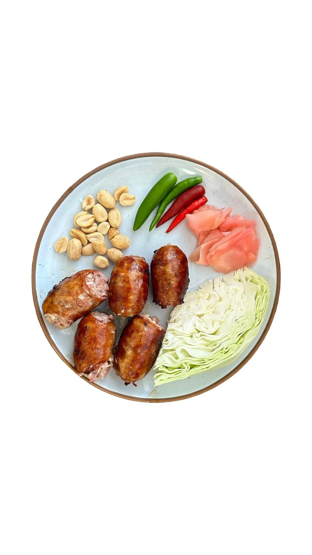 Plate with cooked sausages, peanuts, green and red chili peppers, pickled ginger, and chopped cabbage.