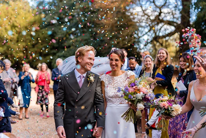 A bridal couple surrounded by colourful confetti after their wedding ceremony
