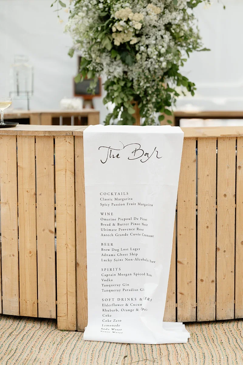 A rustic bar in a marquee for a wedding with a rustic, chic bar menu printed on fabric