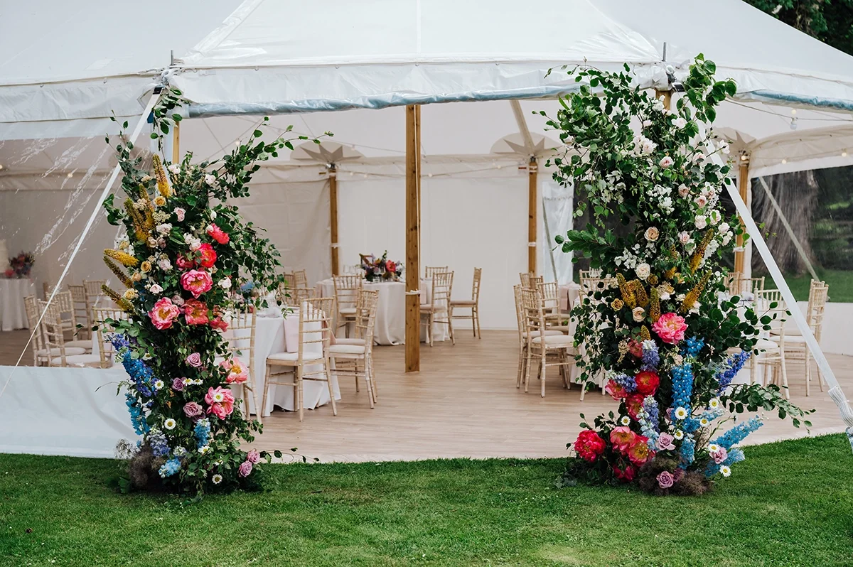 A traditional sailcloth wedding marquee with a floral installation at the entrance