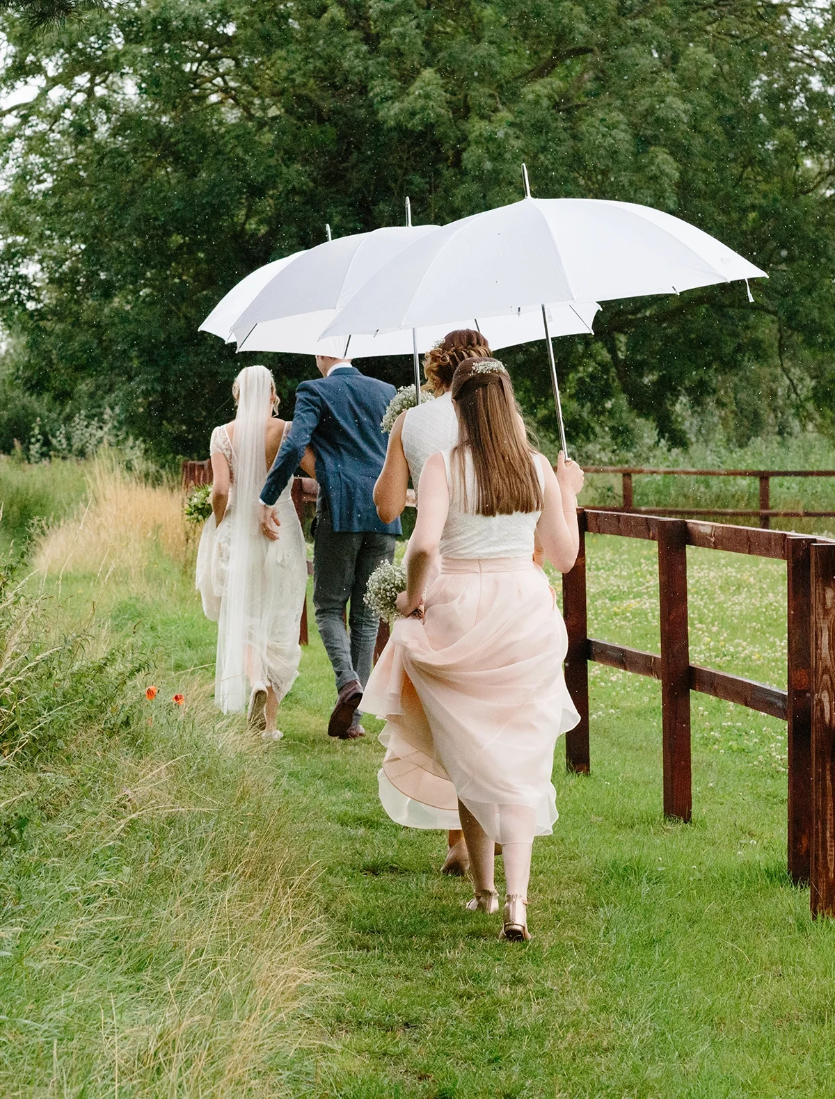 A bride, groom and bridesmaids with umbrellas on a rainy Norfolk wedding day