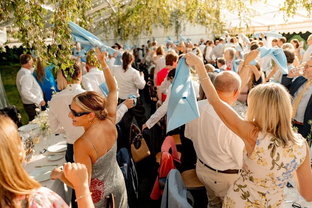 A vibrant wedding reception in a dramatic clear-roofed marquee decorated with foliage