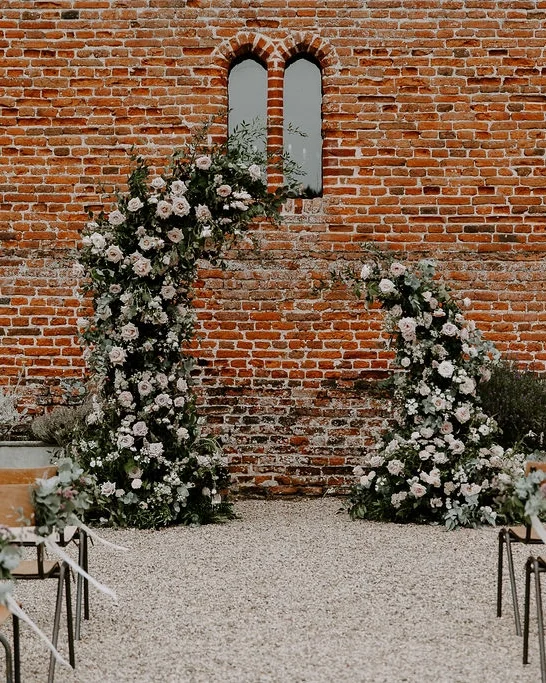A wedding ceremony setup against an ancient brick building with a sculptural floral arch and rustic styling