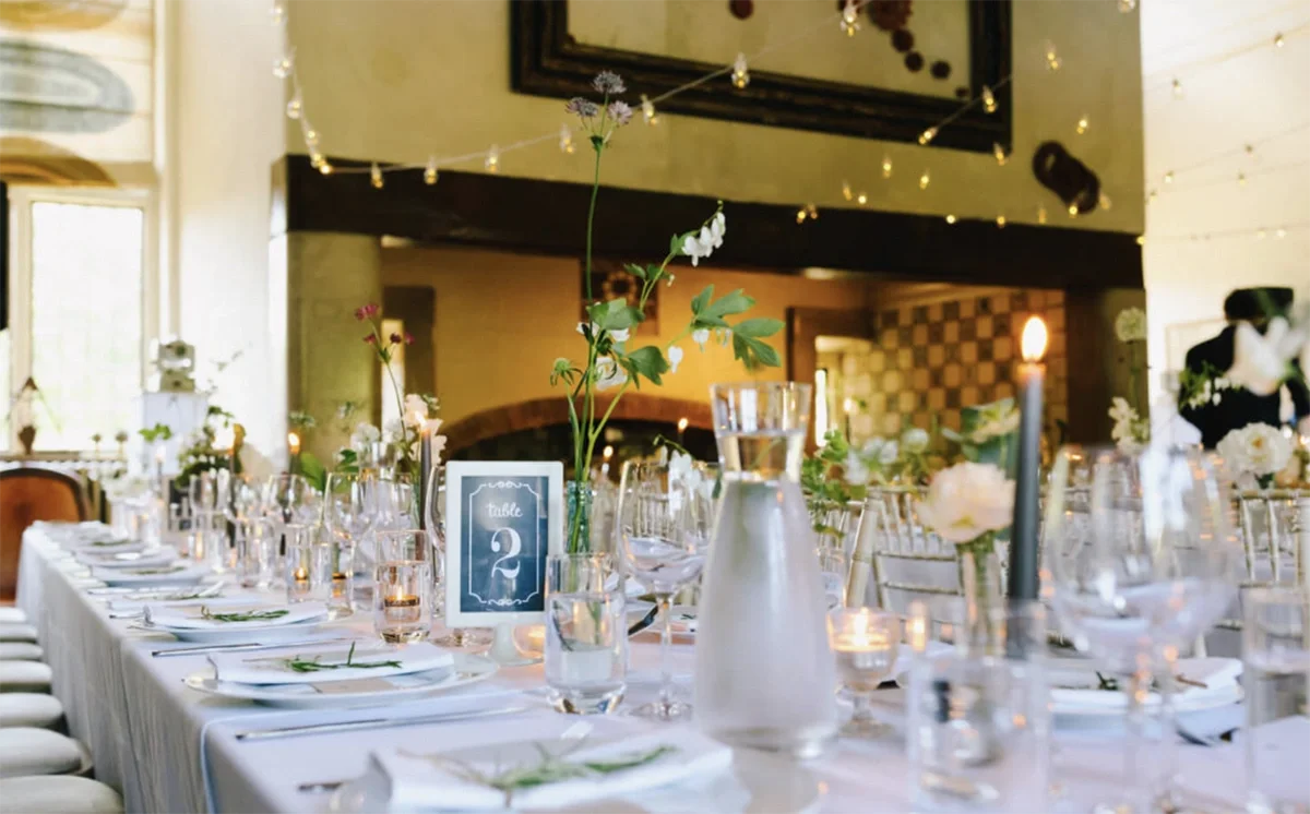 A wedding reception with fairy lights and banqueting tables in the main hall at Voewood