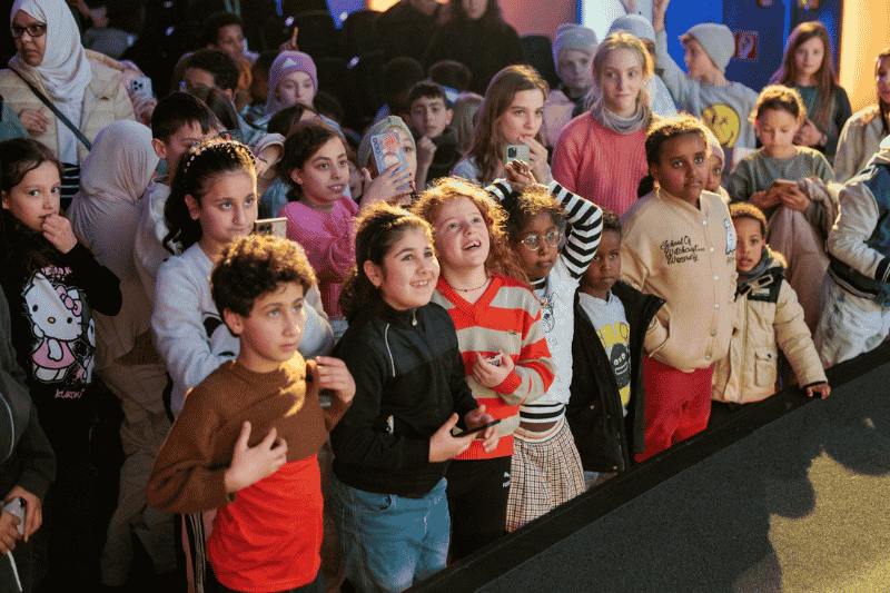 Gruppe von Kindern und Jugendlichen, die einem Schauspiel oder einer Veranstaltung am Empfang zuschauen.