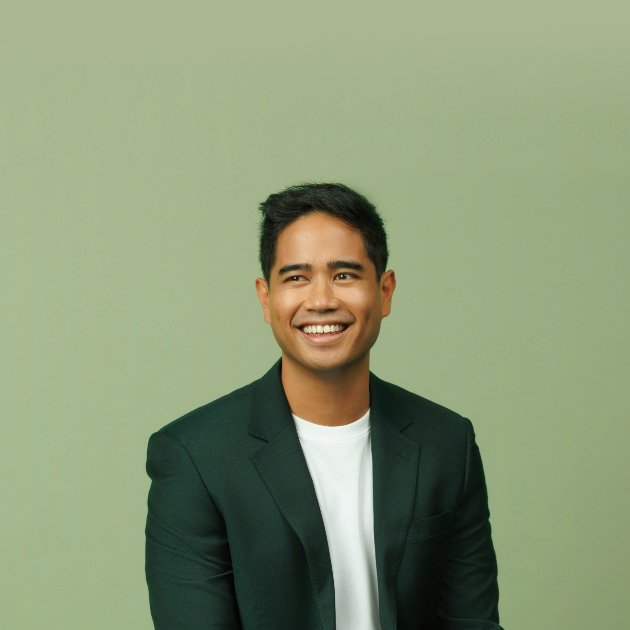 Composer Daniel O’Brien smiling, in a dark green blazer and white T-shirt against a sage green backdrop