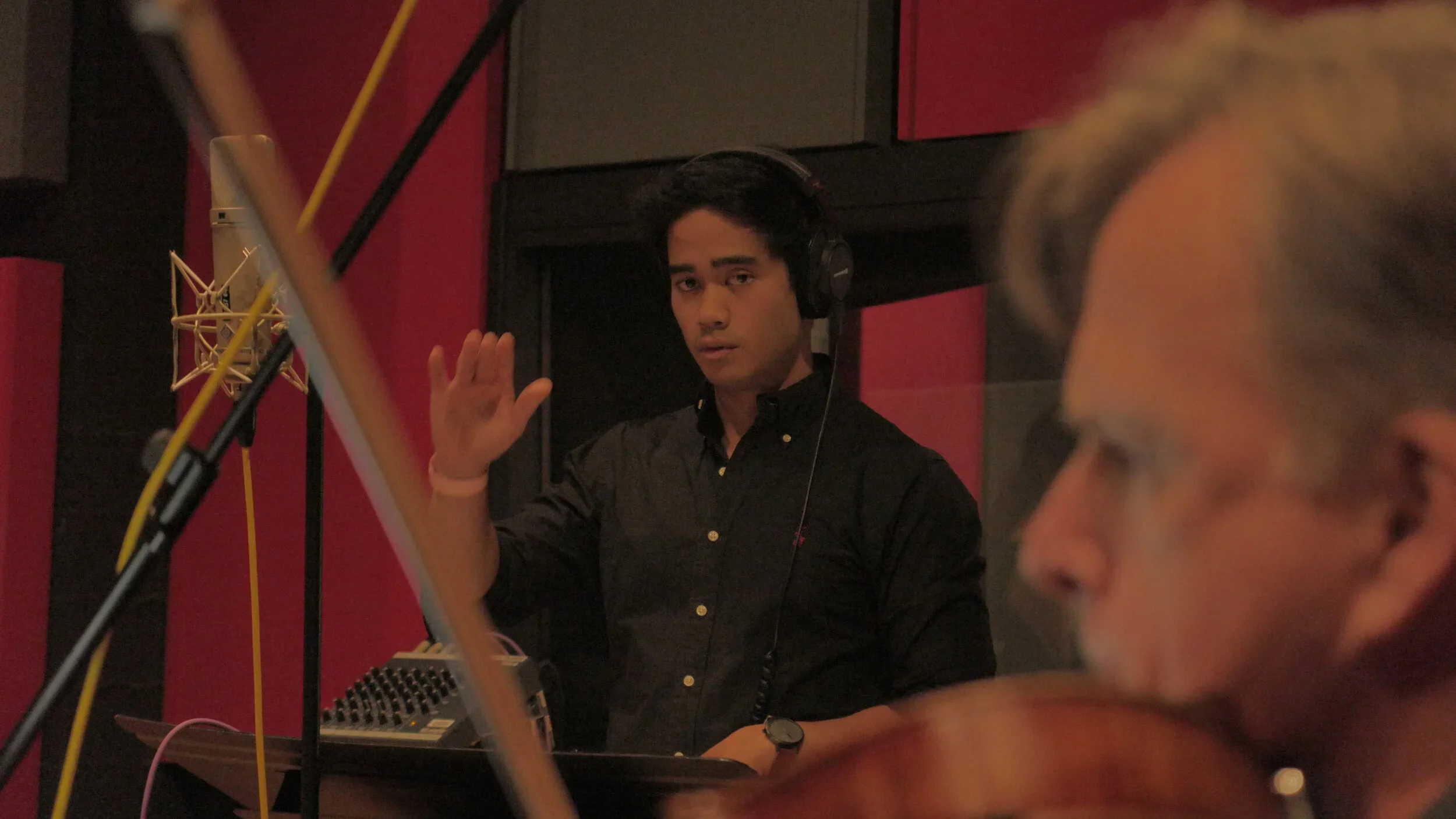 Daniel O’Brien in headphones conducting a string session in a recording studio, with a violinist in the foreground