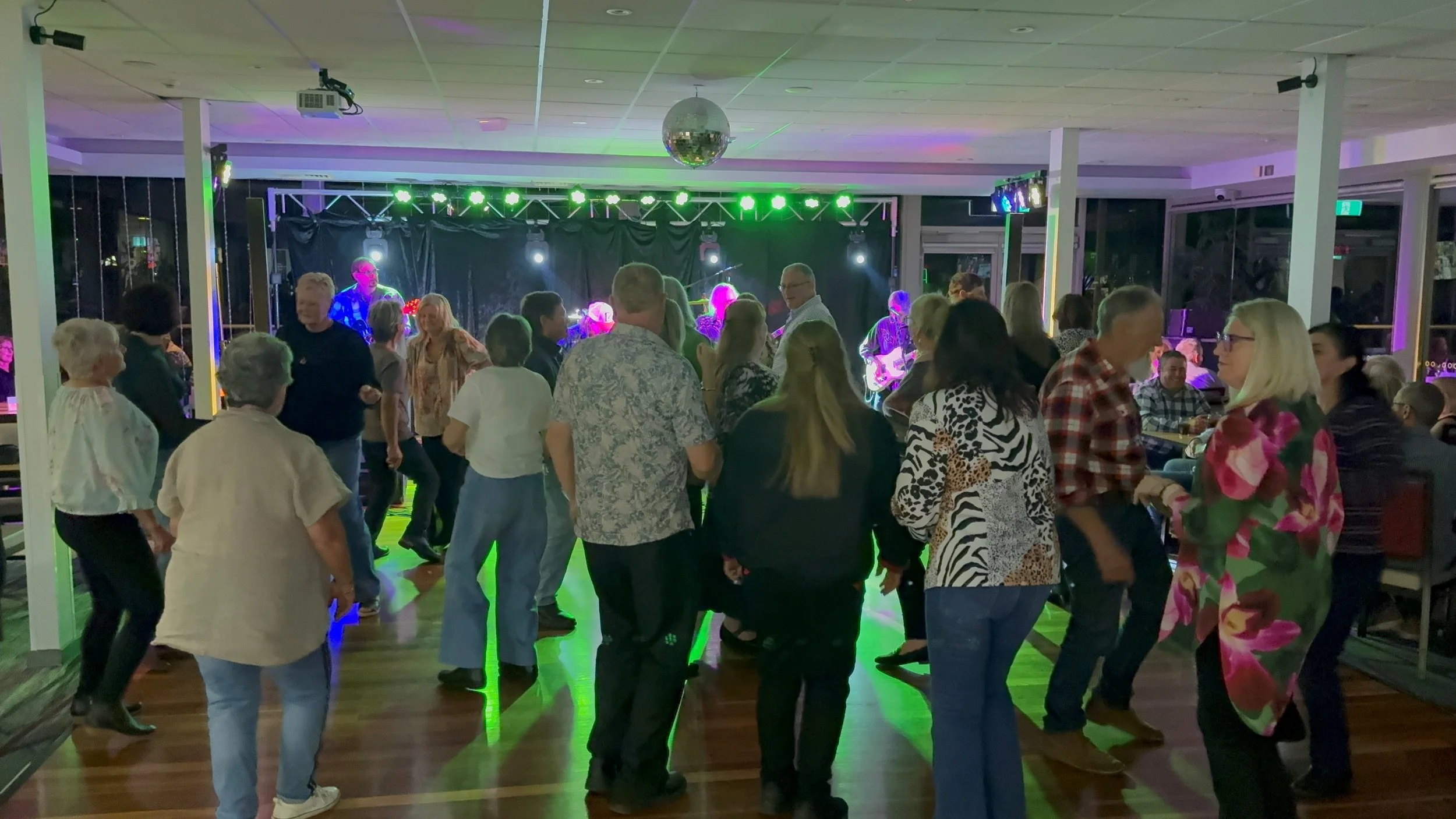 People dancing and socializing at an indoor party with live music and colorful lighting.
