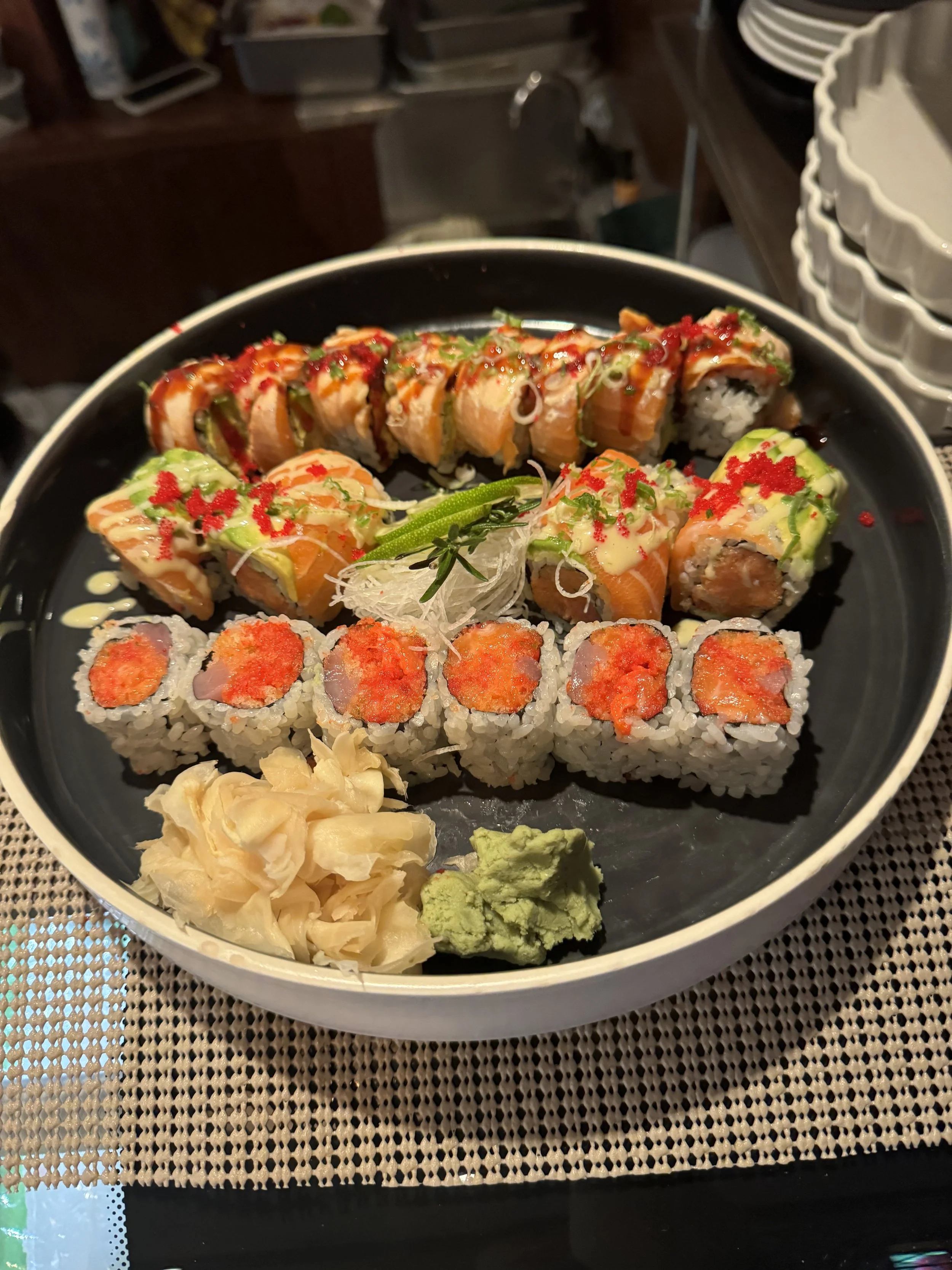 A sushi platter with various types of sushi rolls, wasabi, pickled ginger, and soy sauce on the side.