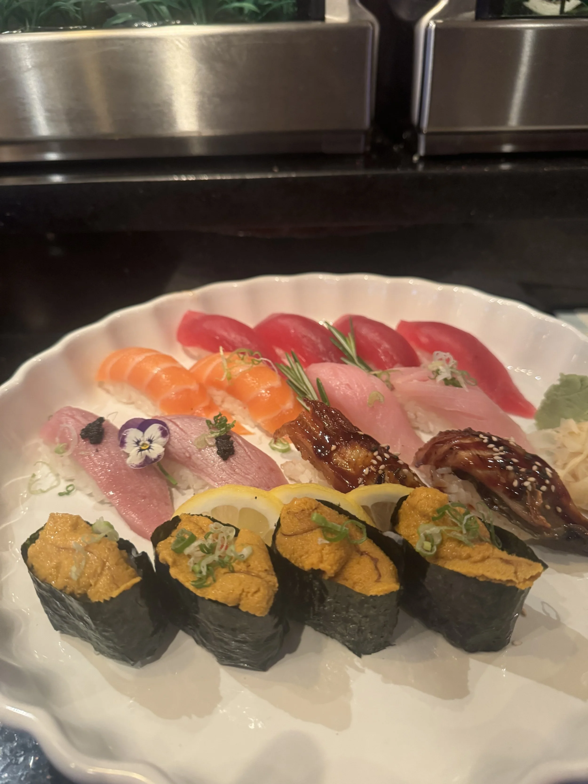 Sushi platter with various types of sushi including slices of raw fish, nigiri, and rolls, decorated with herbs and garnishes.