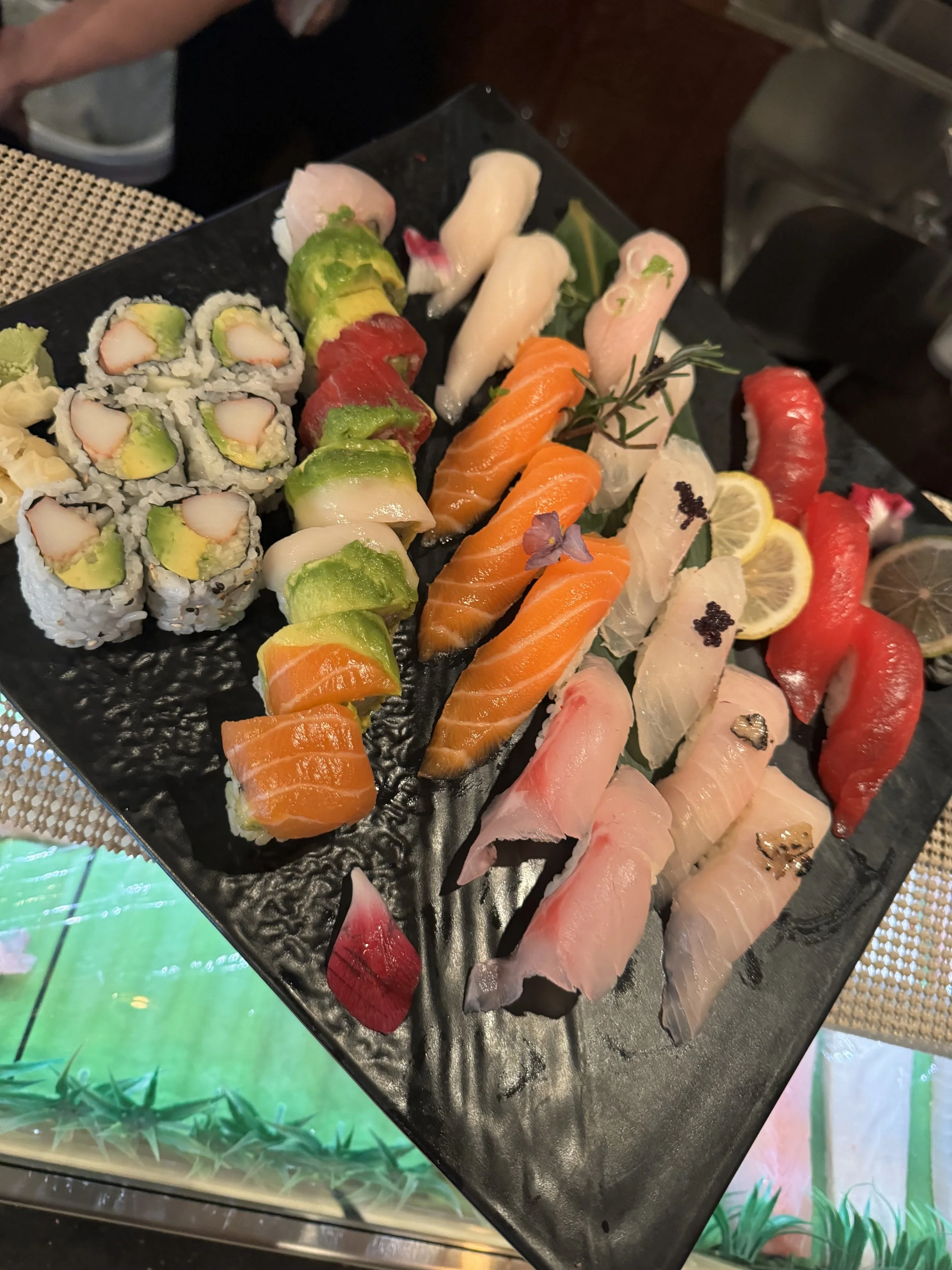 Assorted sushi rolls and sashimi arranged on a black platter, with lemon slices and garnishes.