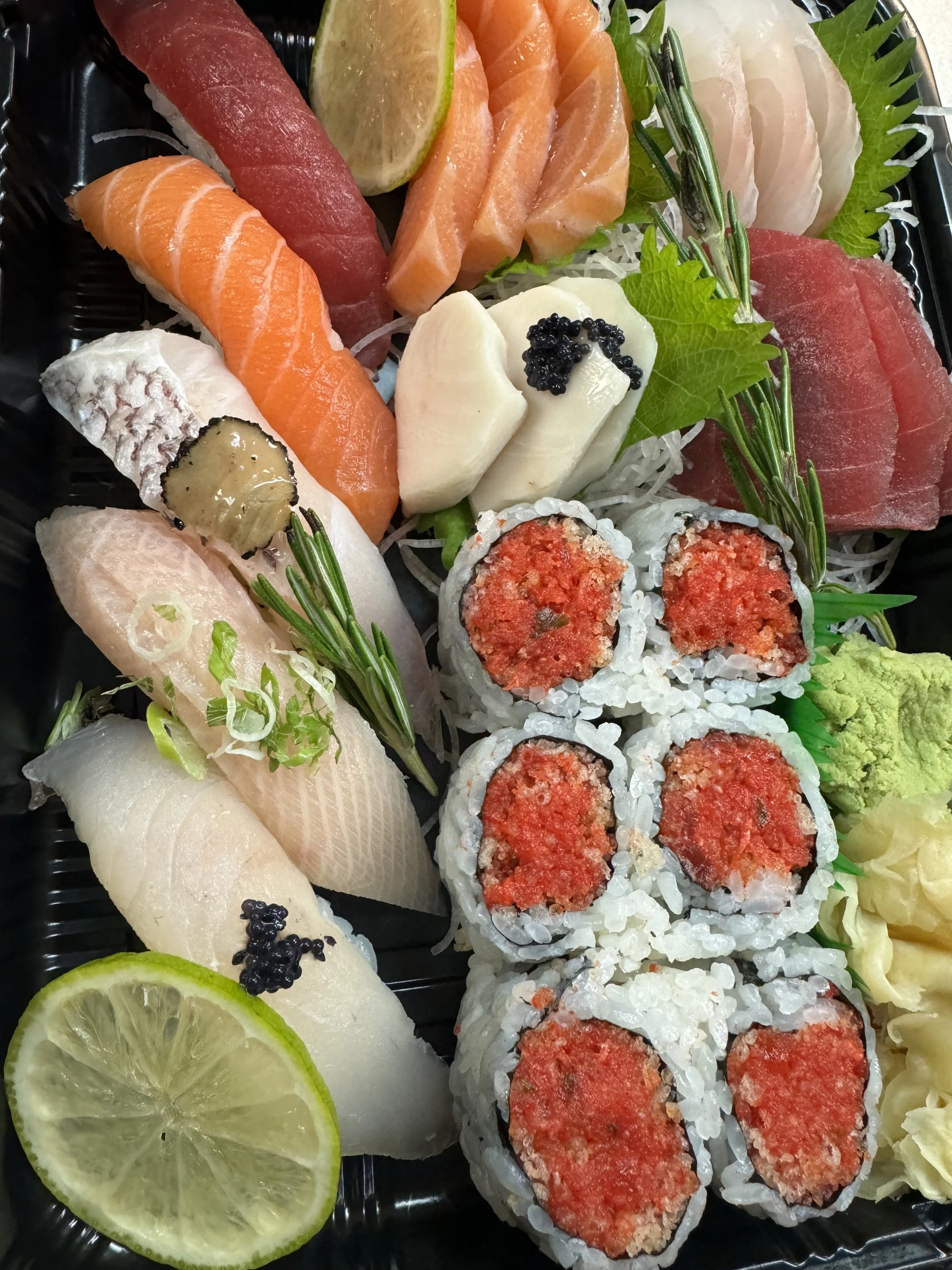 Various types of sashimi and sushi rolls with lemon and lime slices, garnished with herbs and wasabi.
