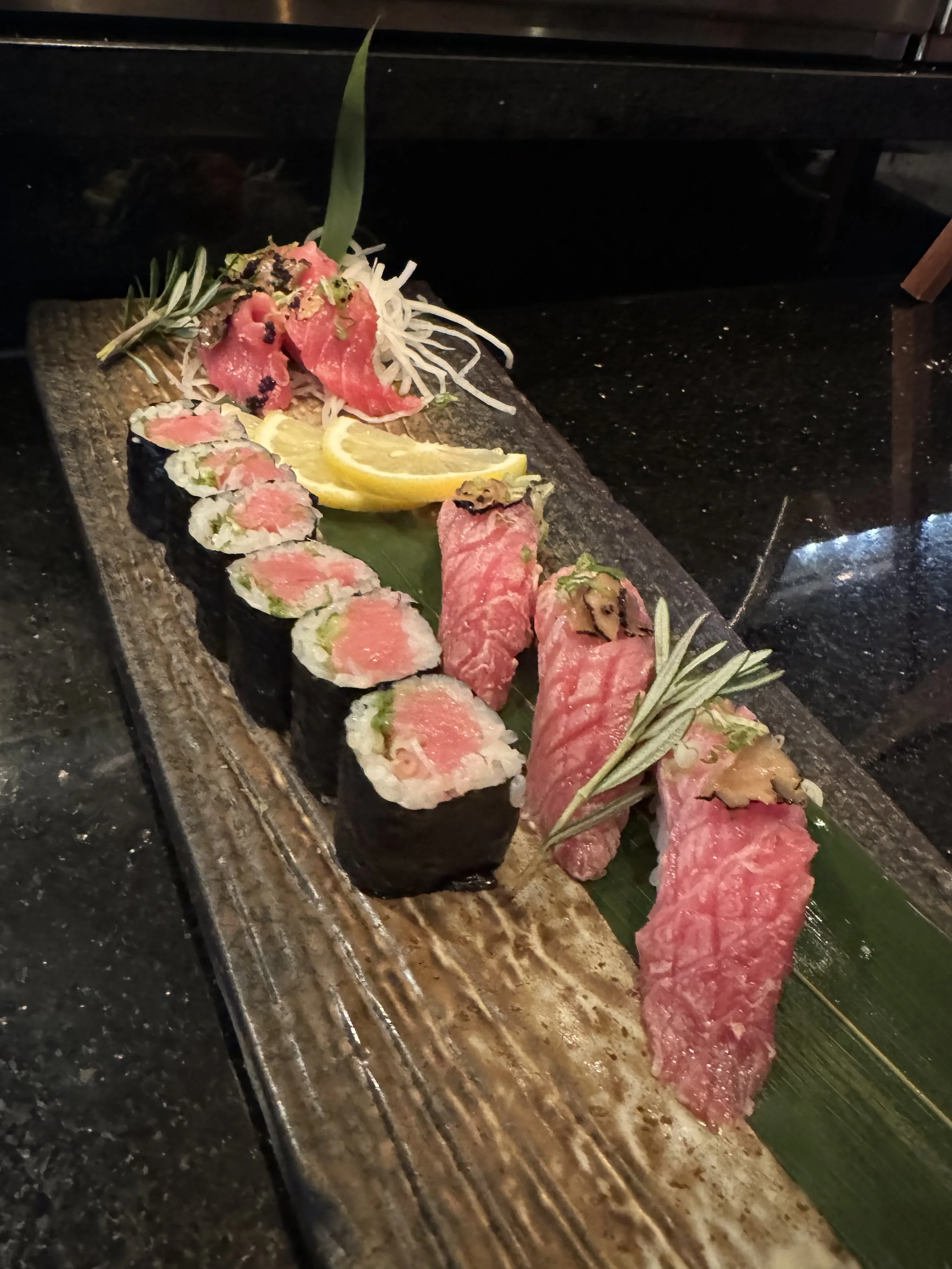 Sushi or sashimi platter with slices of raw fish, garnished with lemon slices, herbs, and shredded vegetables on a ceramic plate.