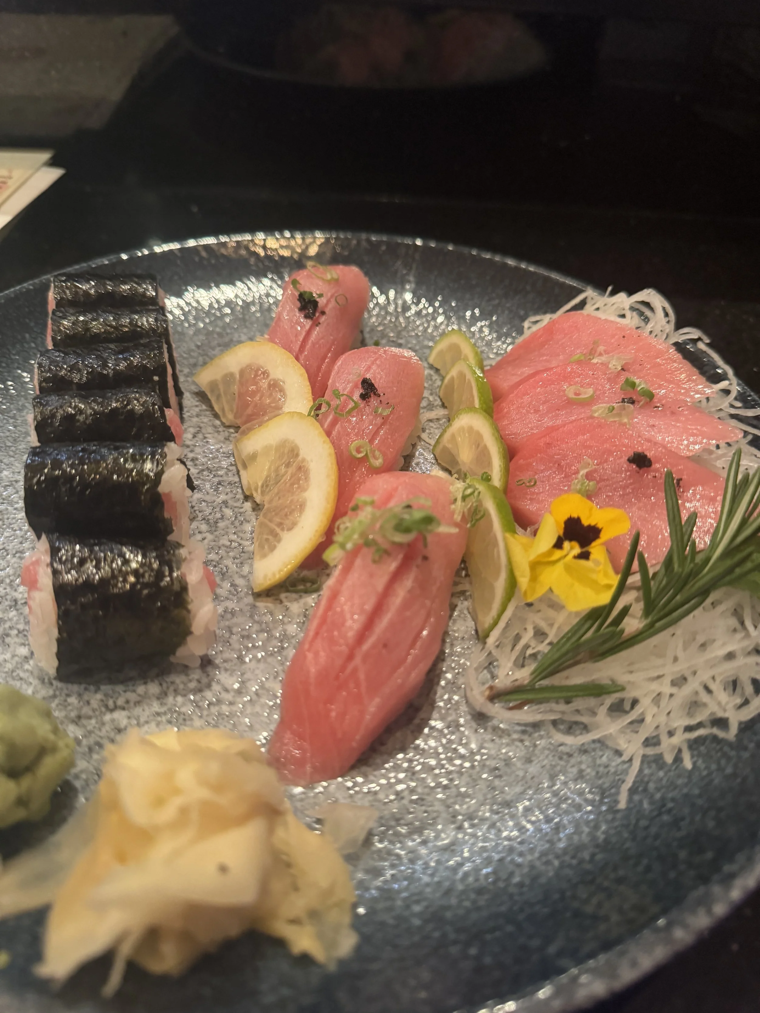Sashimi platter with slices of raw fish, lemon and lime wedges, garnished with flowers and herbs on a decorative plate.