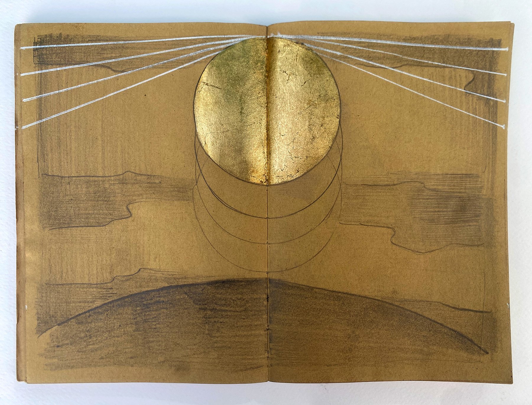 Open sketchbook with gold leaf circle and geometric lines, with faint line drawings and shading beneath.