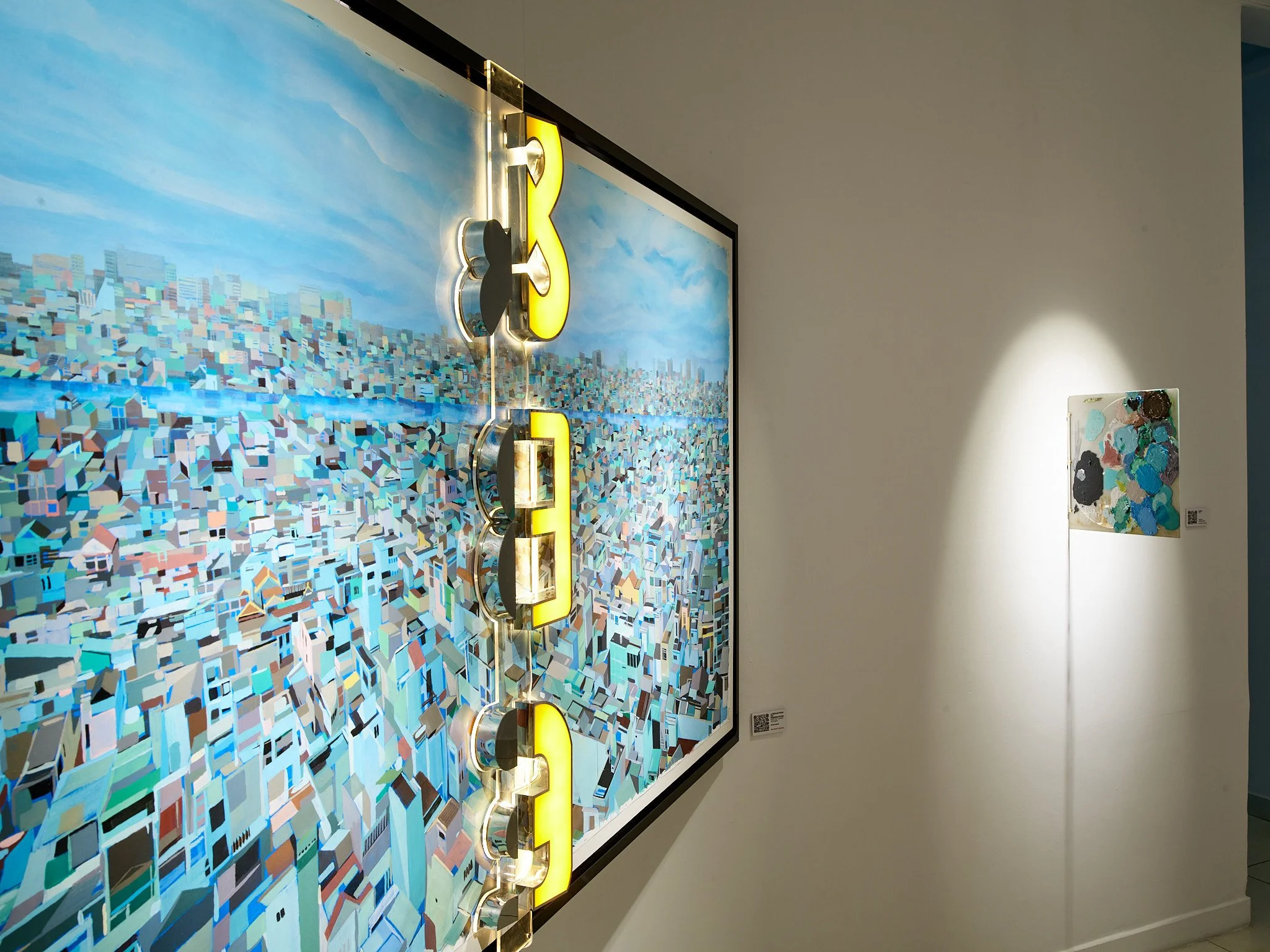 blue painting of rooftops with yellow sign and small abstract painting on the side