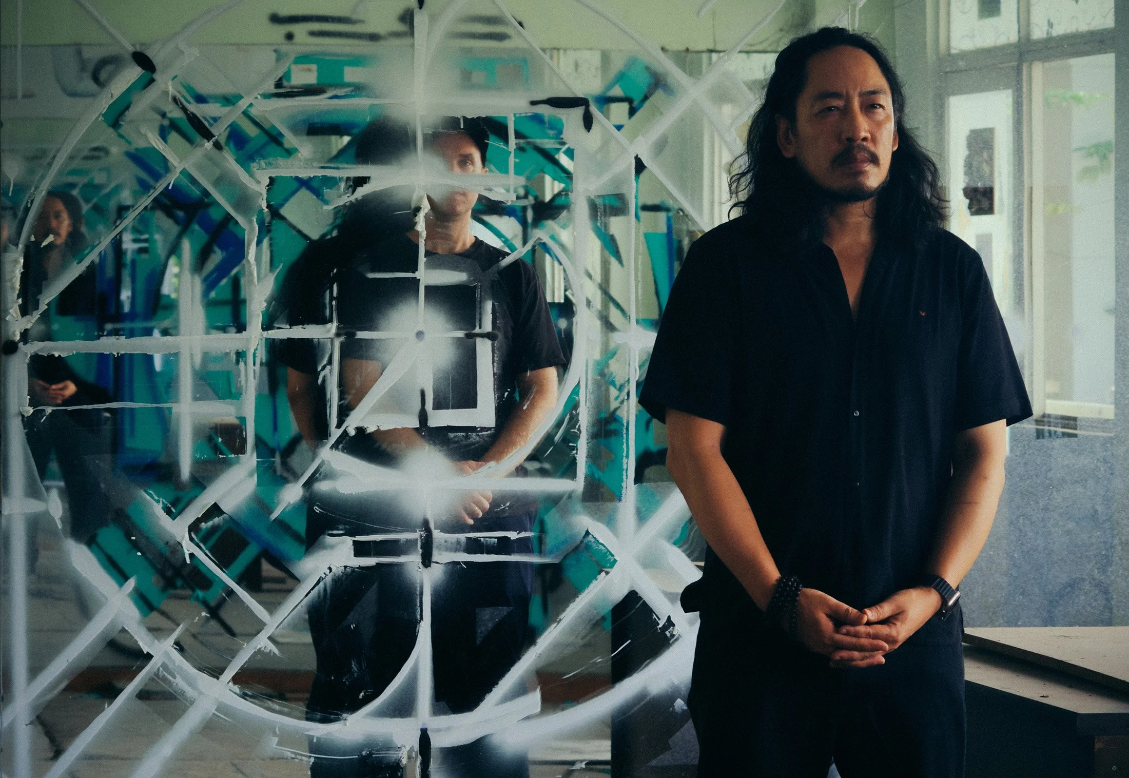 two men posed in front of an abstract geometric mandala painted on a mirror with spray paint in an abandoned room