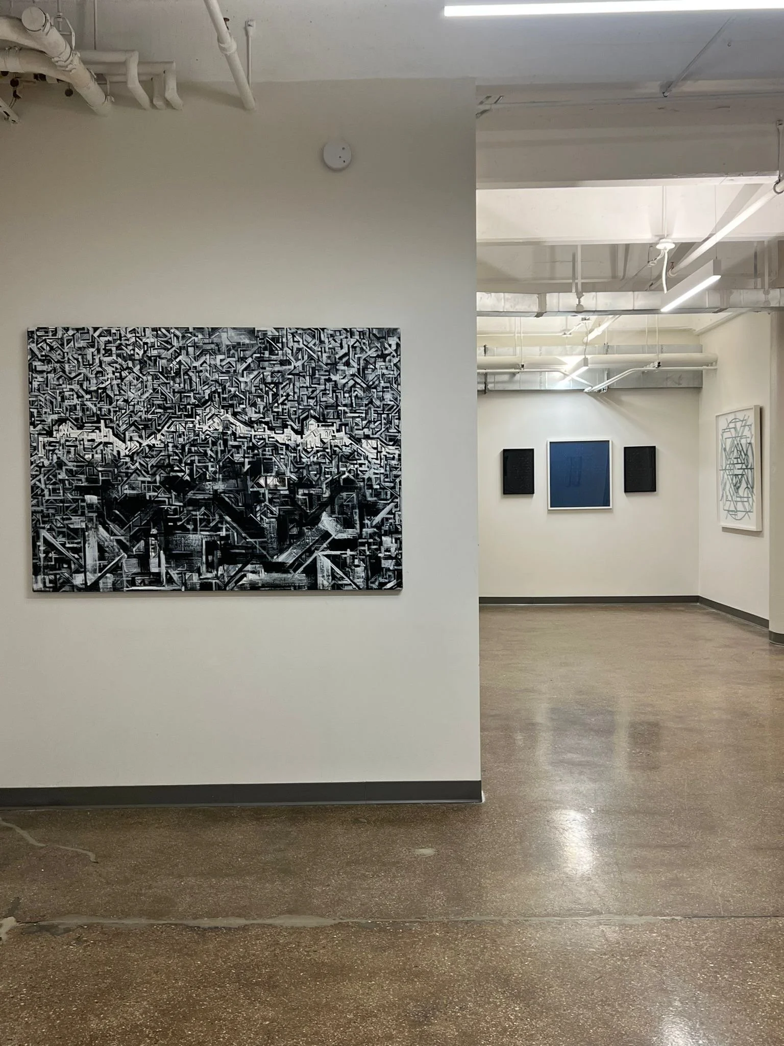 gallery space with black and white cityscape in the foreground and geometric pieces behind