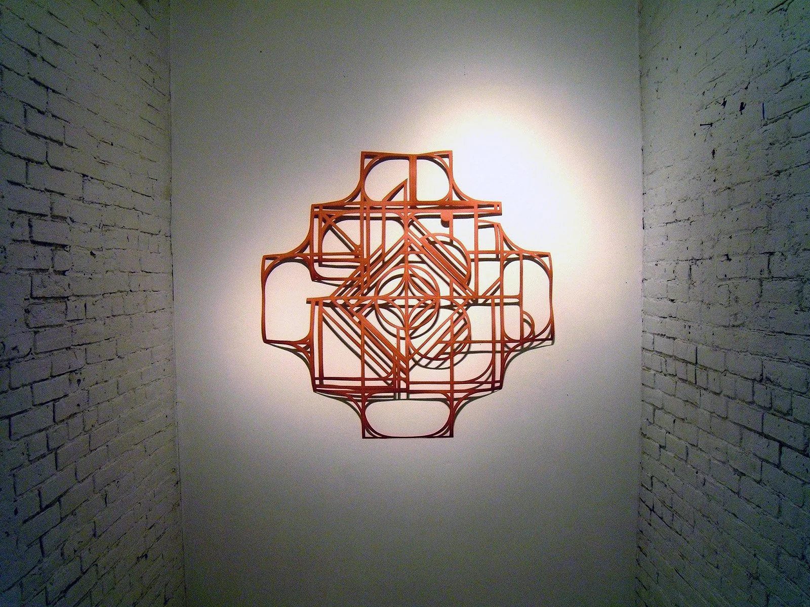 abstract geometric mandala artwork from cut orange paper casting a shadow on a gallery wall